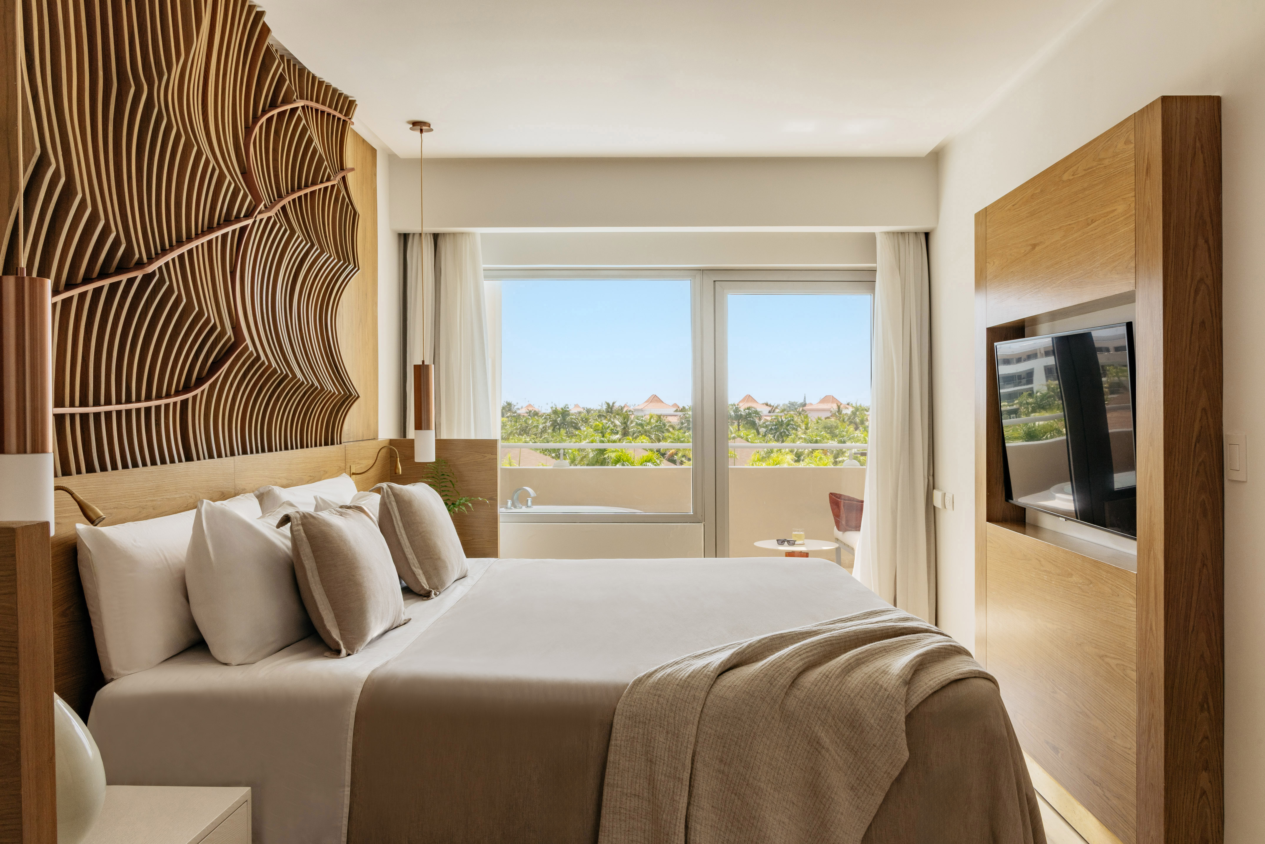 Luxury hotel room with king bed, wavy wooden headboard, tropical view.