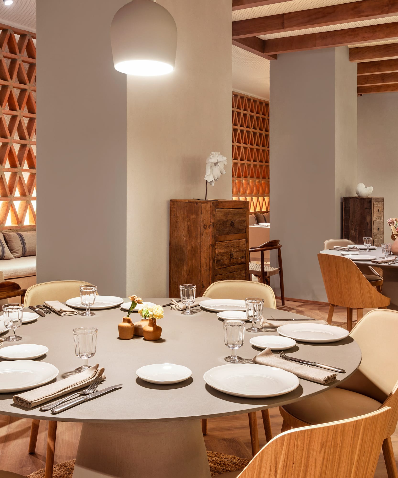 Modern restaurant dining room with round tables, wooden chairs, and terracotta screen.