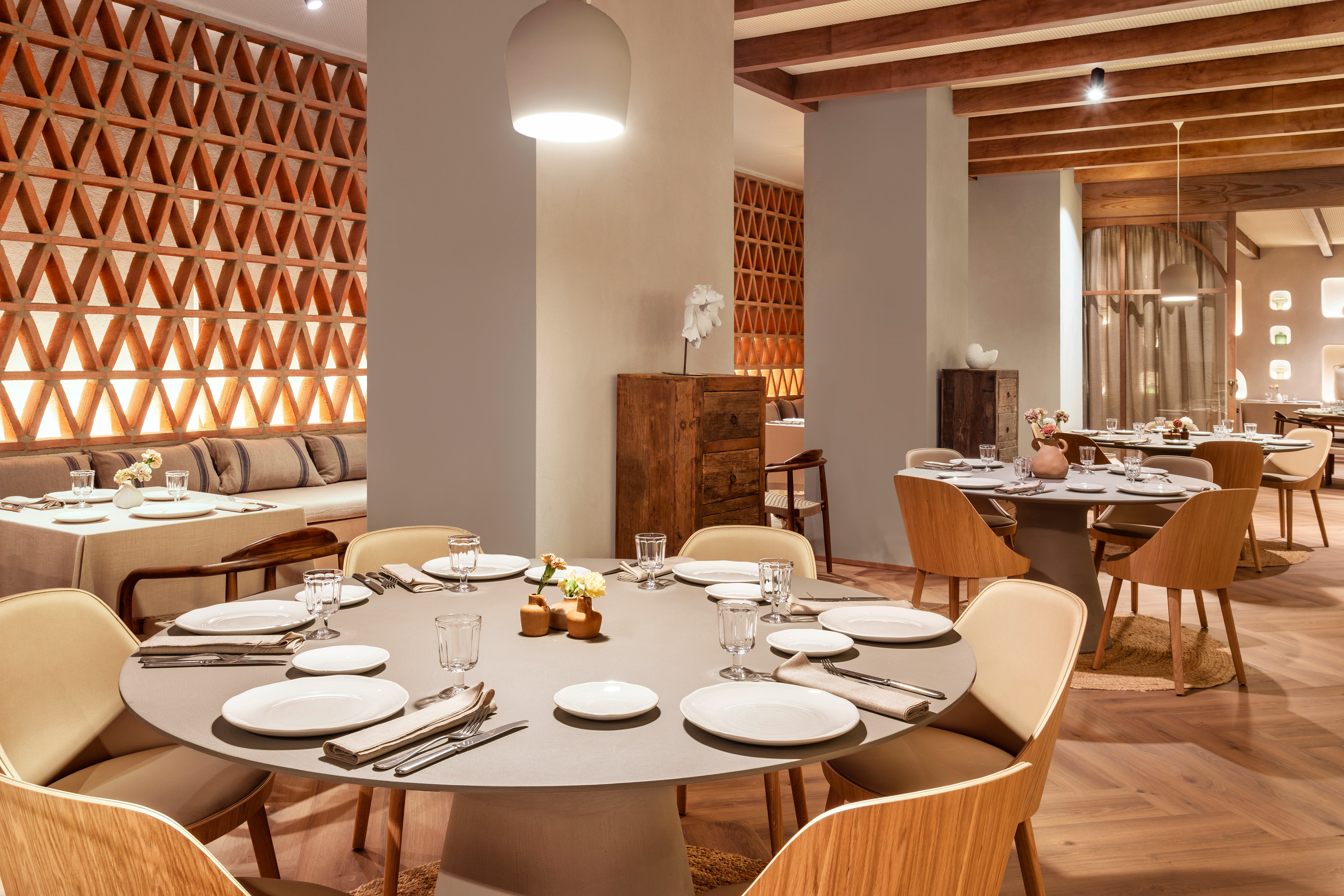 Modern restaurant dining room with round tables, wooden chairs, and terracotta screen.
