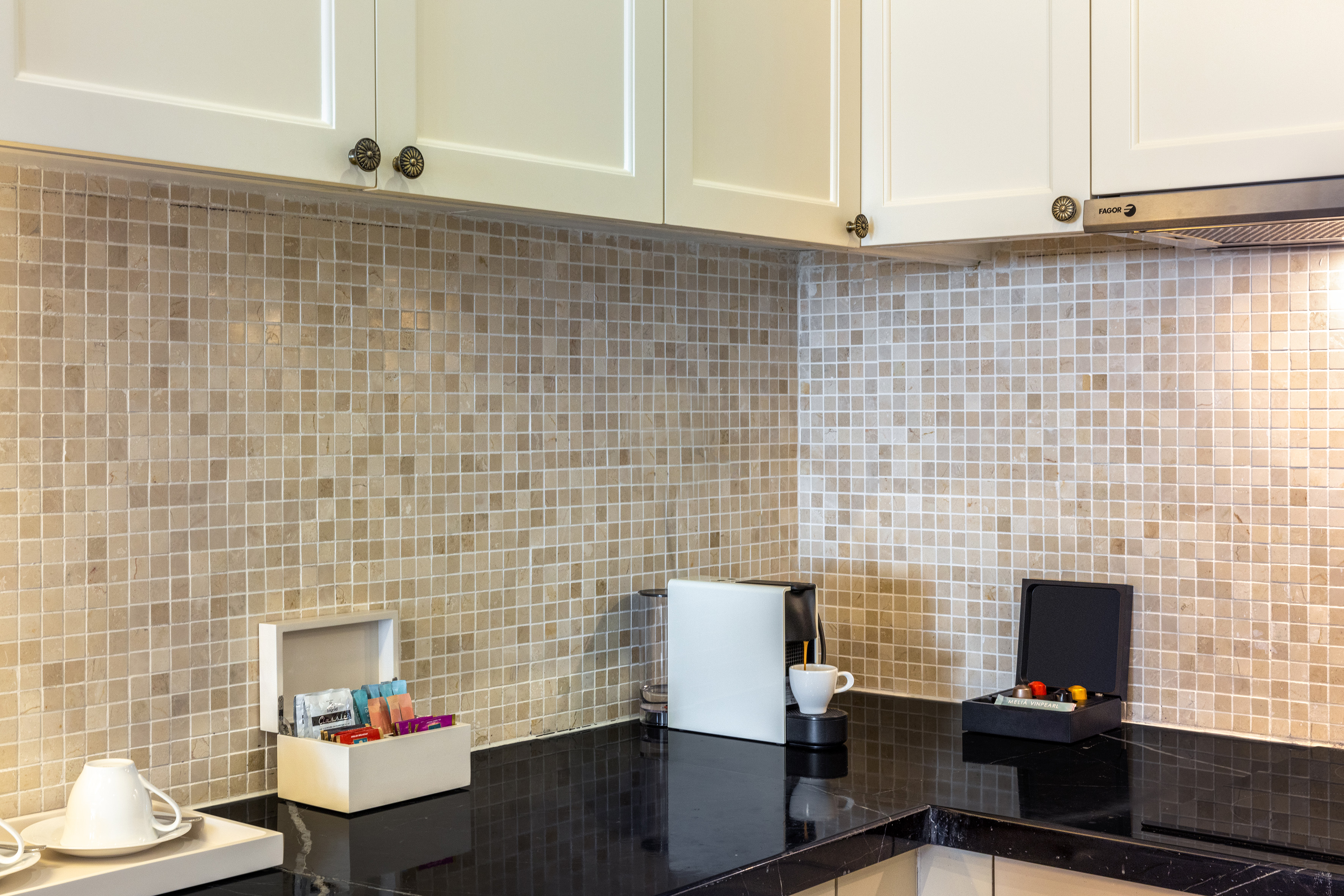 Hotel kitchenette with coffee machine, tea, and mosaic tile backsplash.