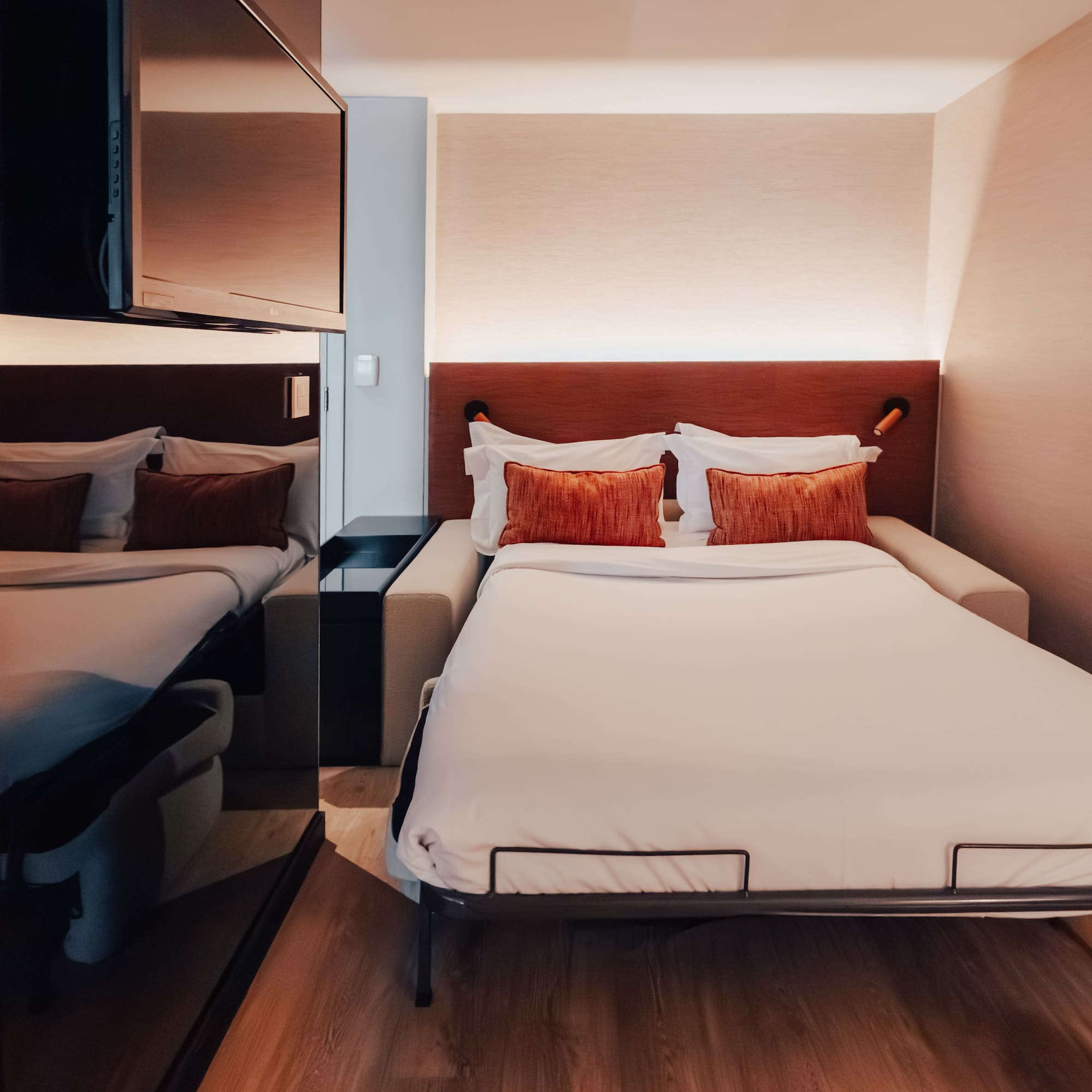 Modern hotel room with pull-out bed, white bedding, and orange pillows.
