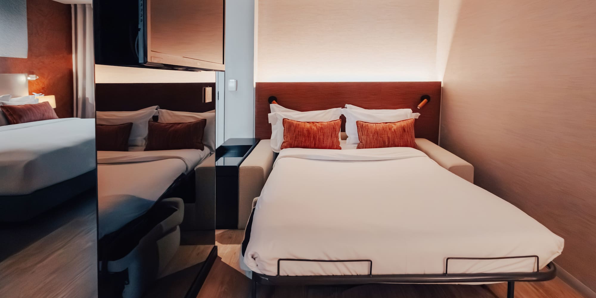 Modern hotel room with pull-out bed, white bedding, and orange pillows.