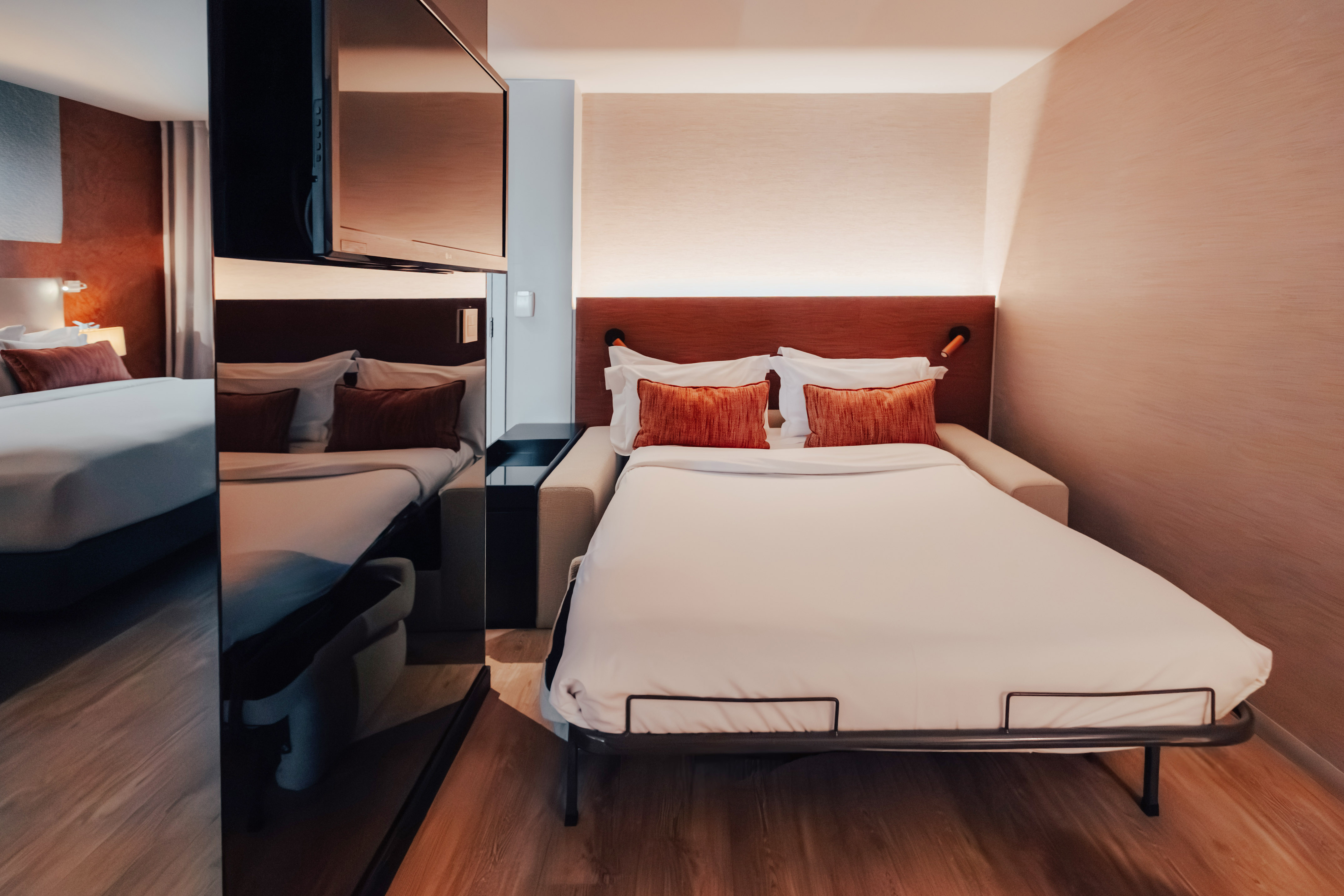 Modern hotel room with pull-out bed, white bedding, and orange pillows.