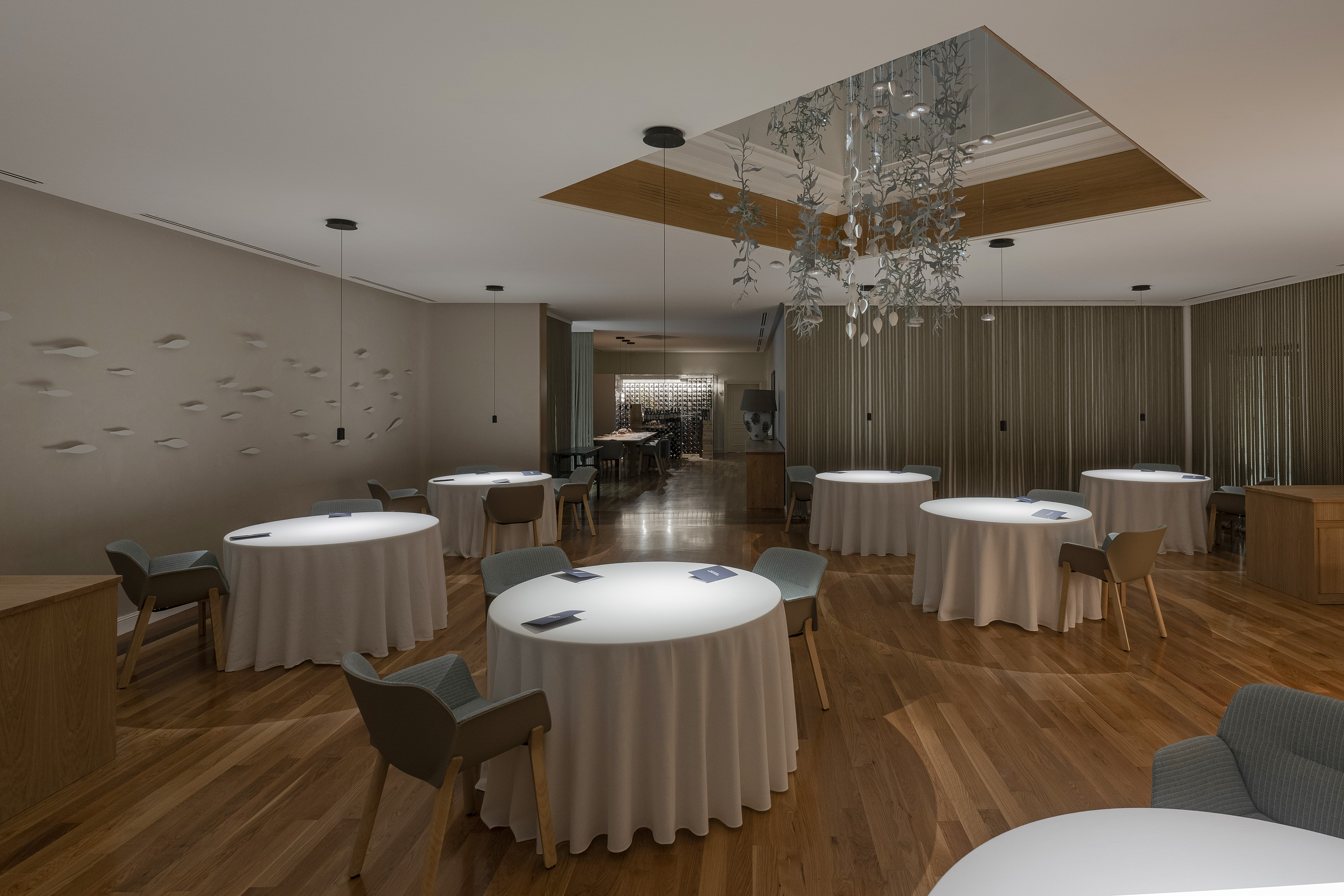 Elegant restaurant dining room, round tables, wood floor, contemporary lighting.