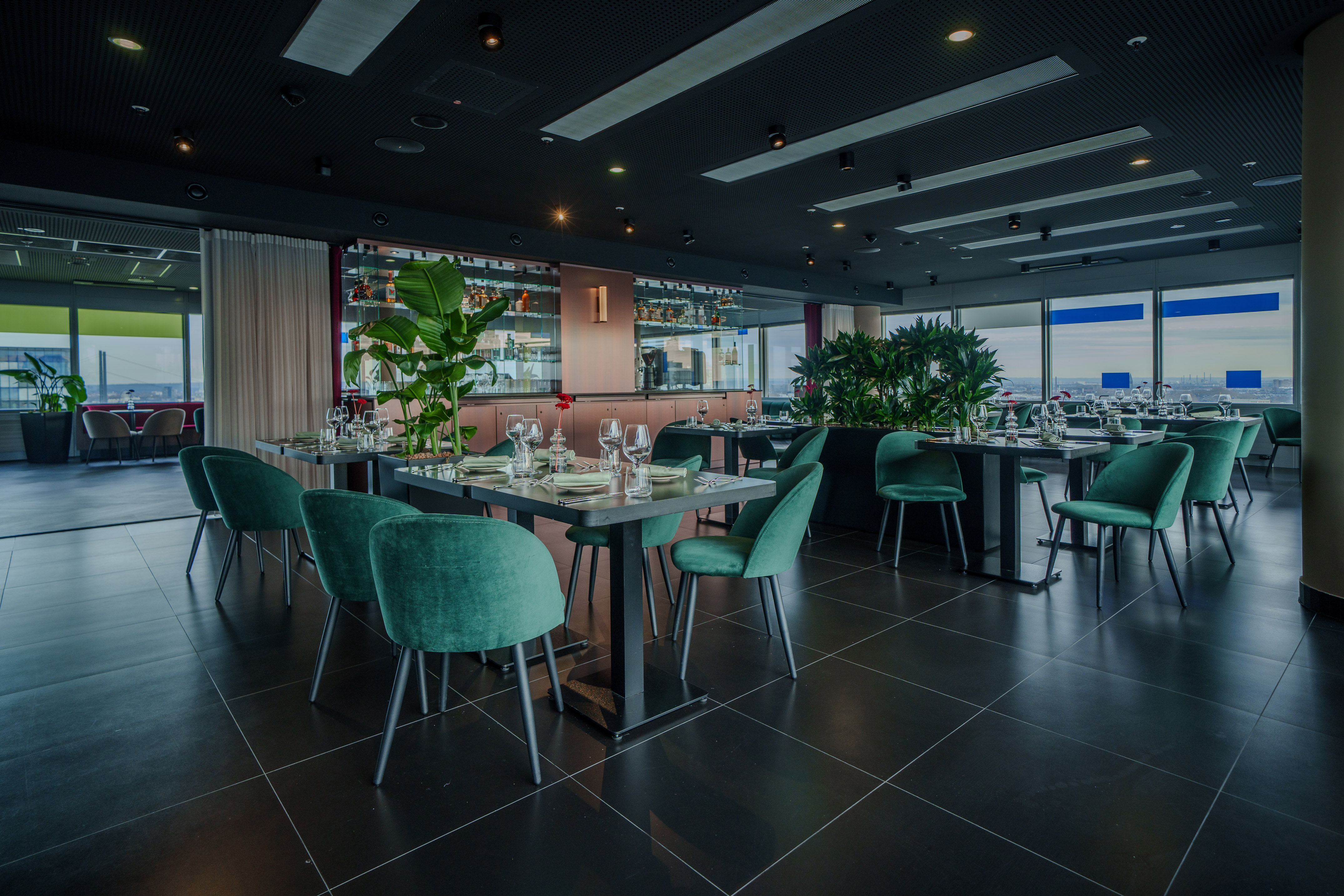 Contemporary restaurant with teal velvet dining chairs, bar, and city view.