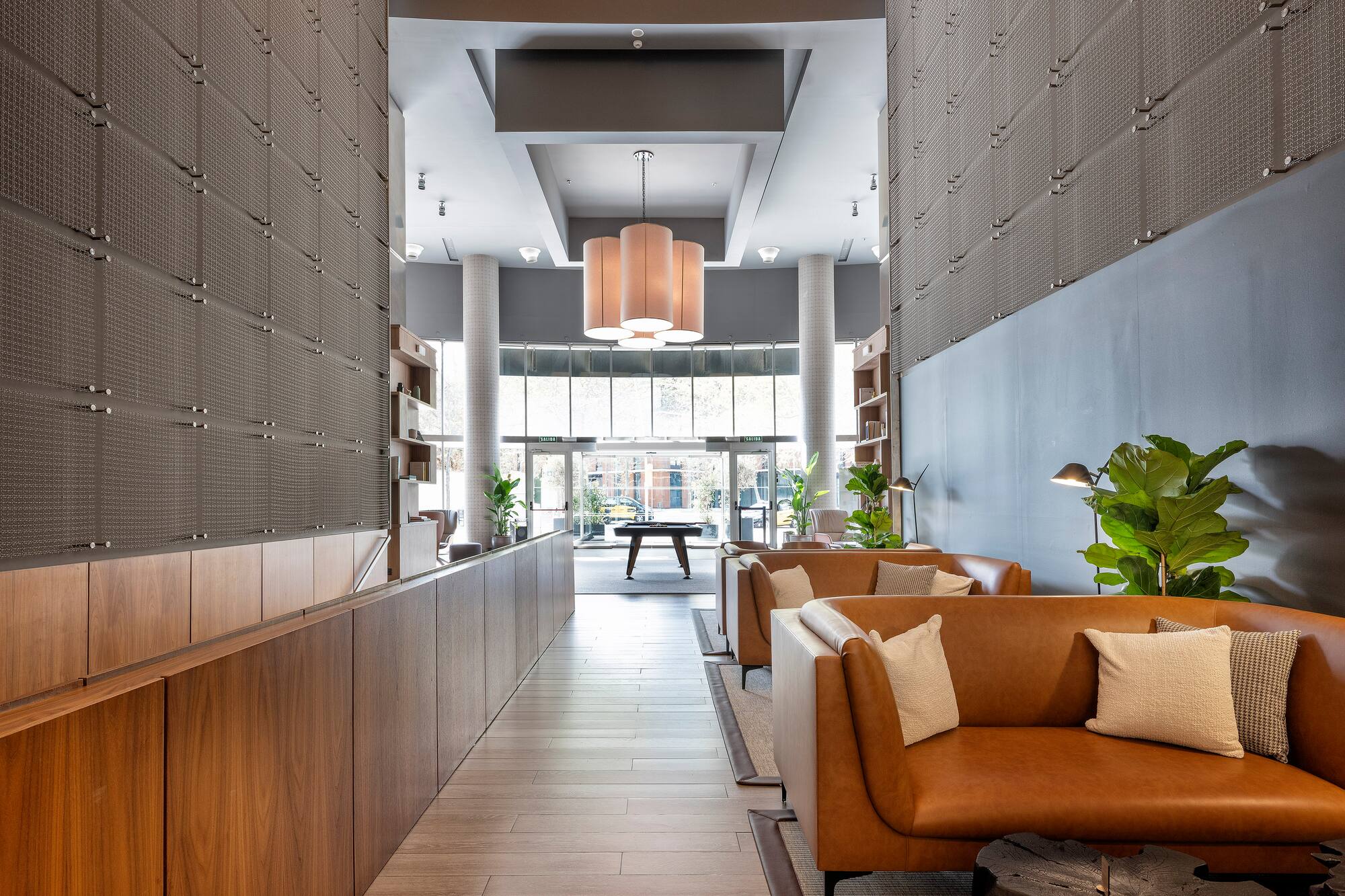 Modern lobby lounge with brown leather sofas, wood walls, and hanging lights.