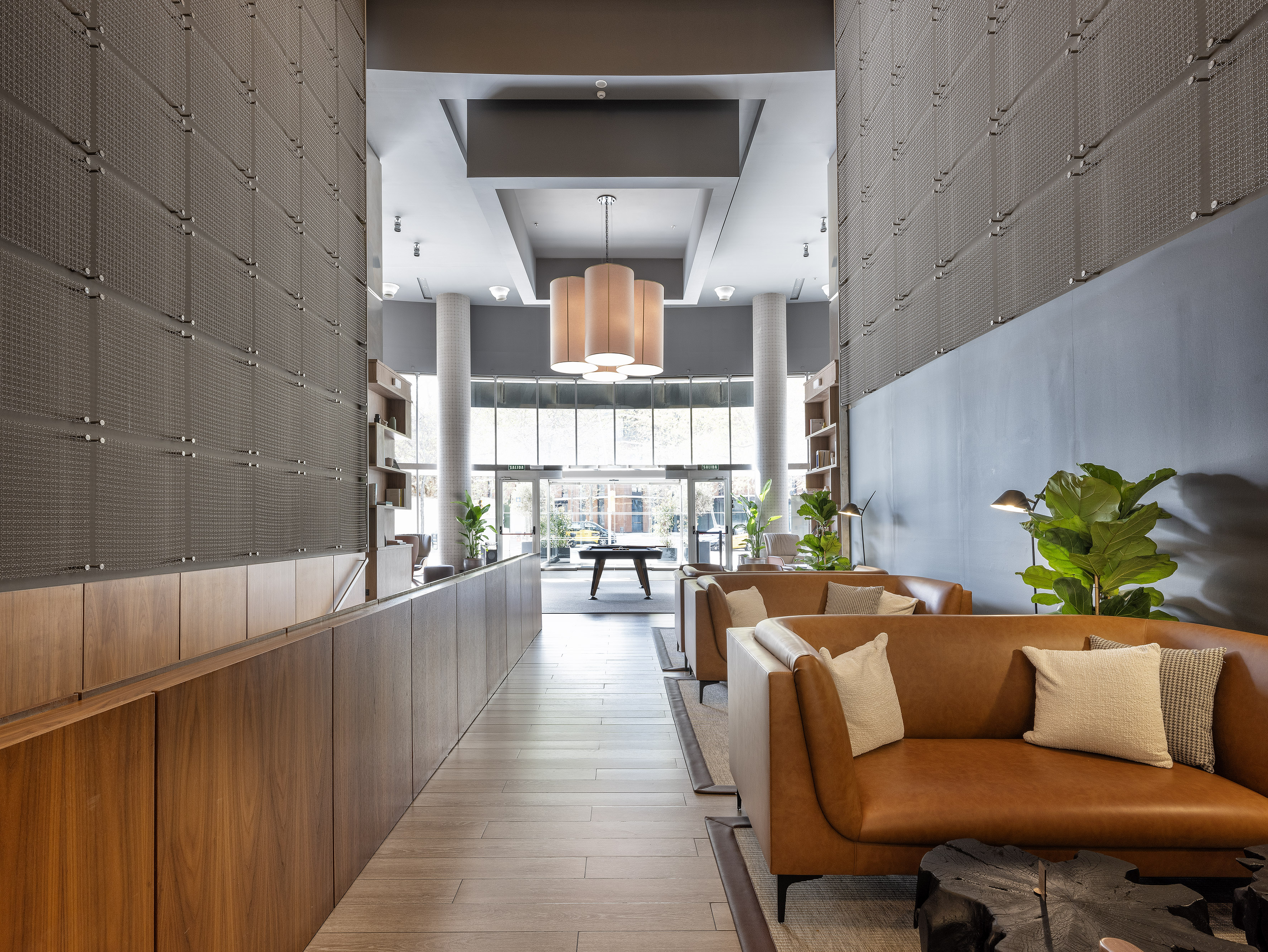 Modern lobby lounge with brown leather sofas, wood walls, and hanging lights.