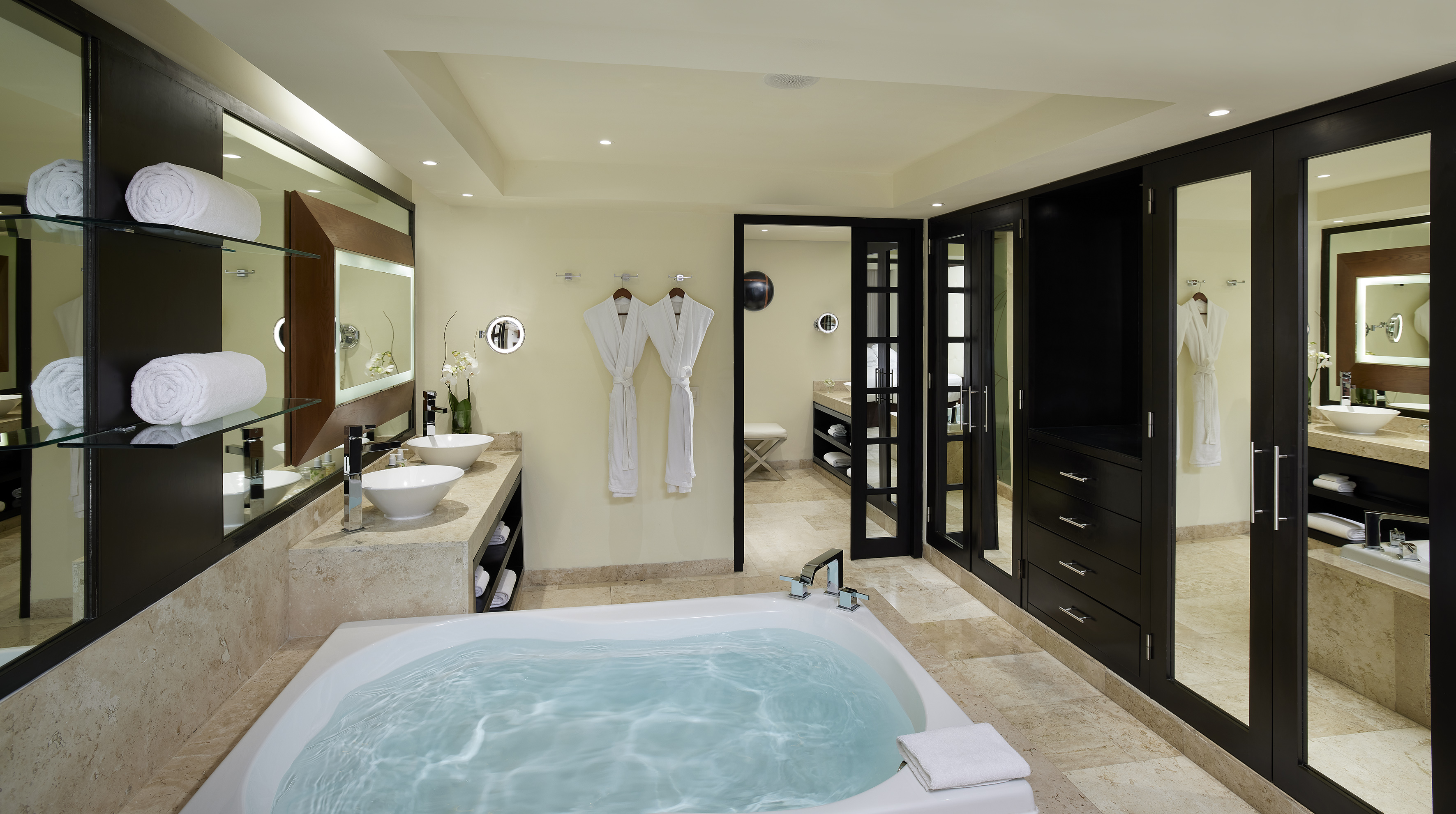 Elegant hotel bathroom with large soaking tub, double sinks, and white bathrobes.