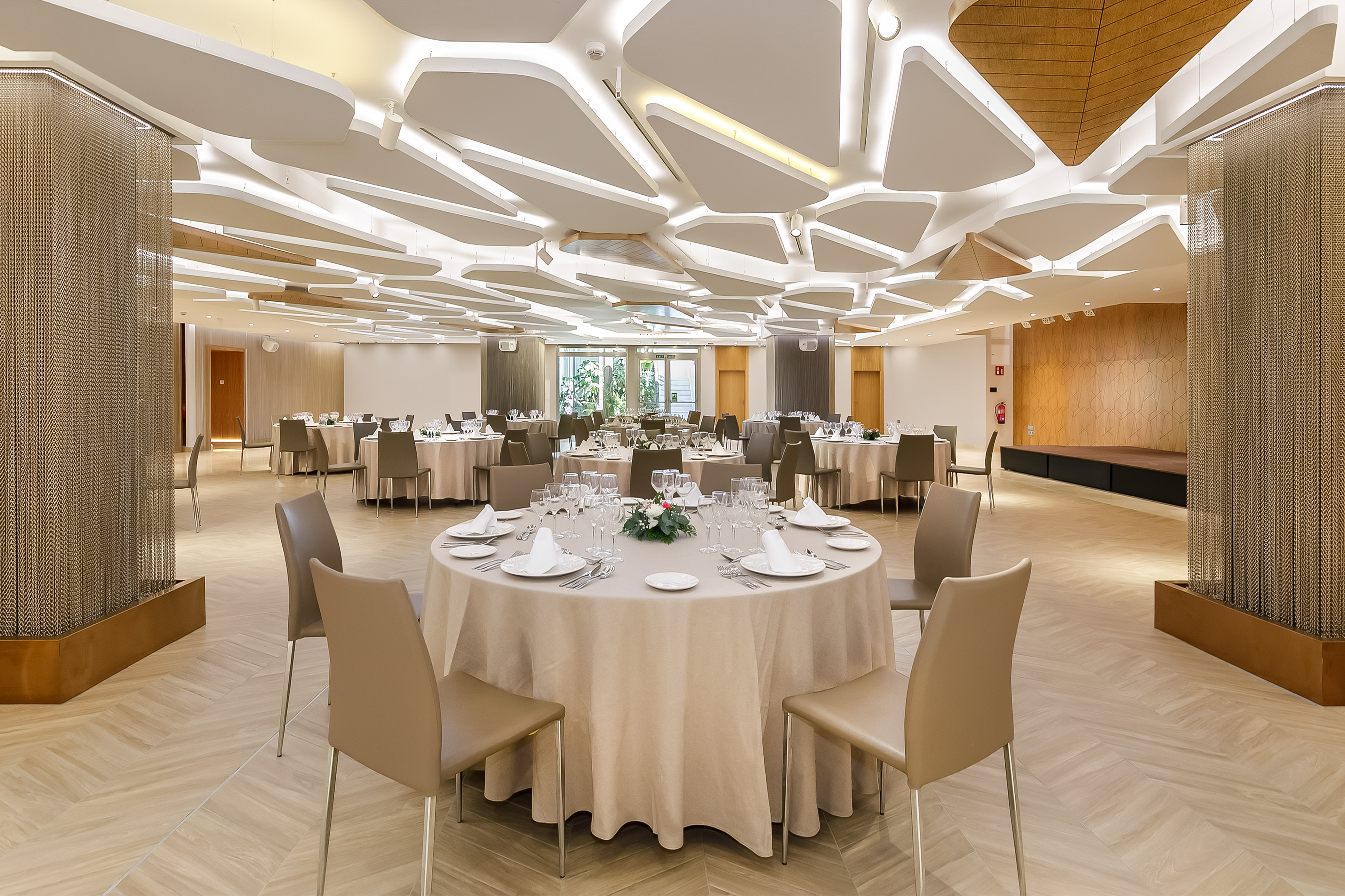 Elegant modern banquet hall with set tables, geometric ceiling, and warm lighting.