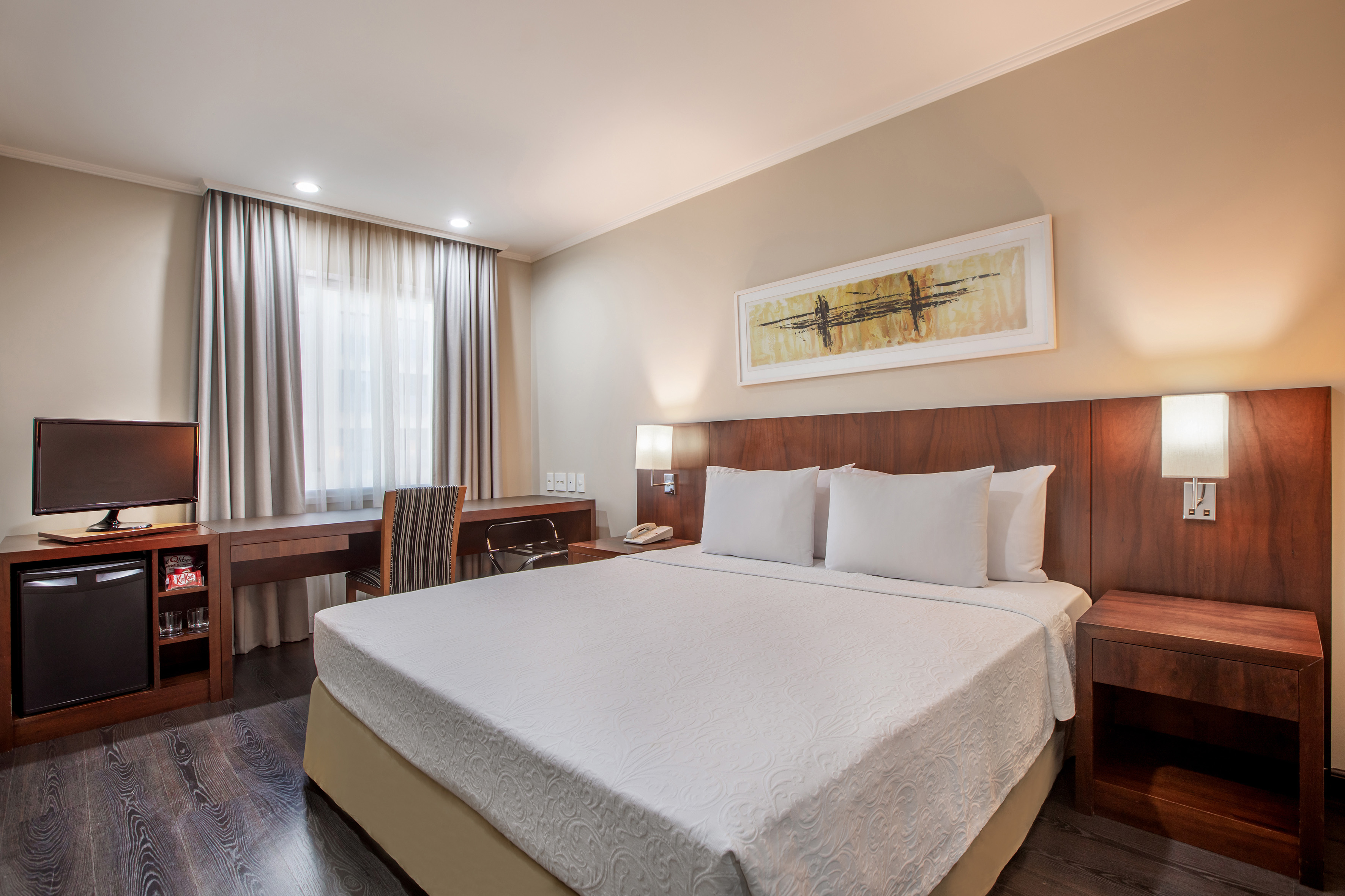 Modern hotel room with queen bed, desk, TV, and mini-fridge.