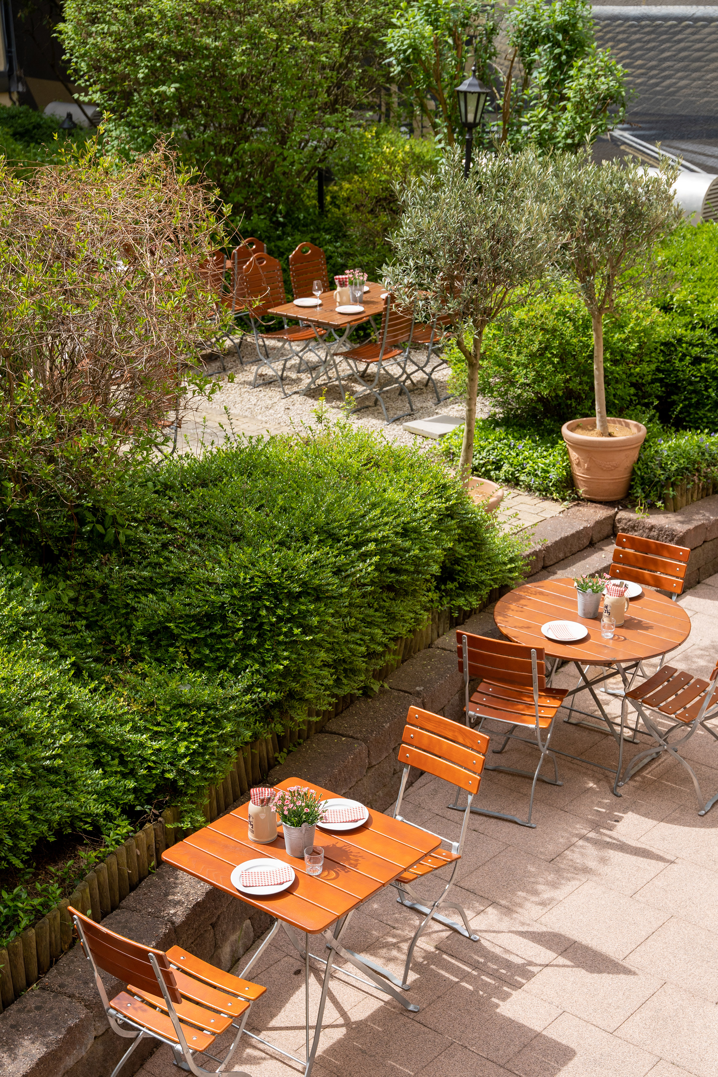 Outdoor cafe garden patio with wooden tables, chairs, and lush greenery.