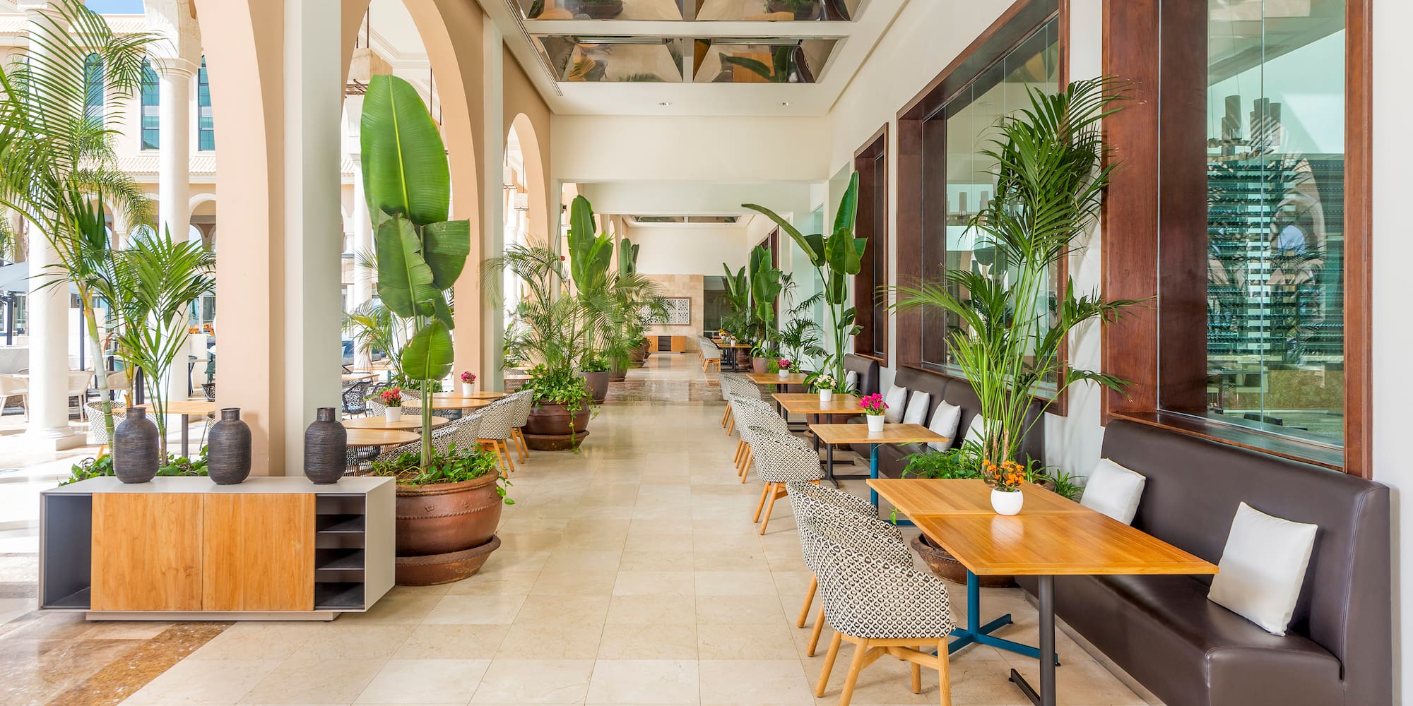 Tropical resort dining area with lush plants, modern tables, and arched architecture.