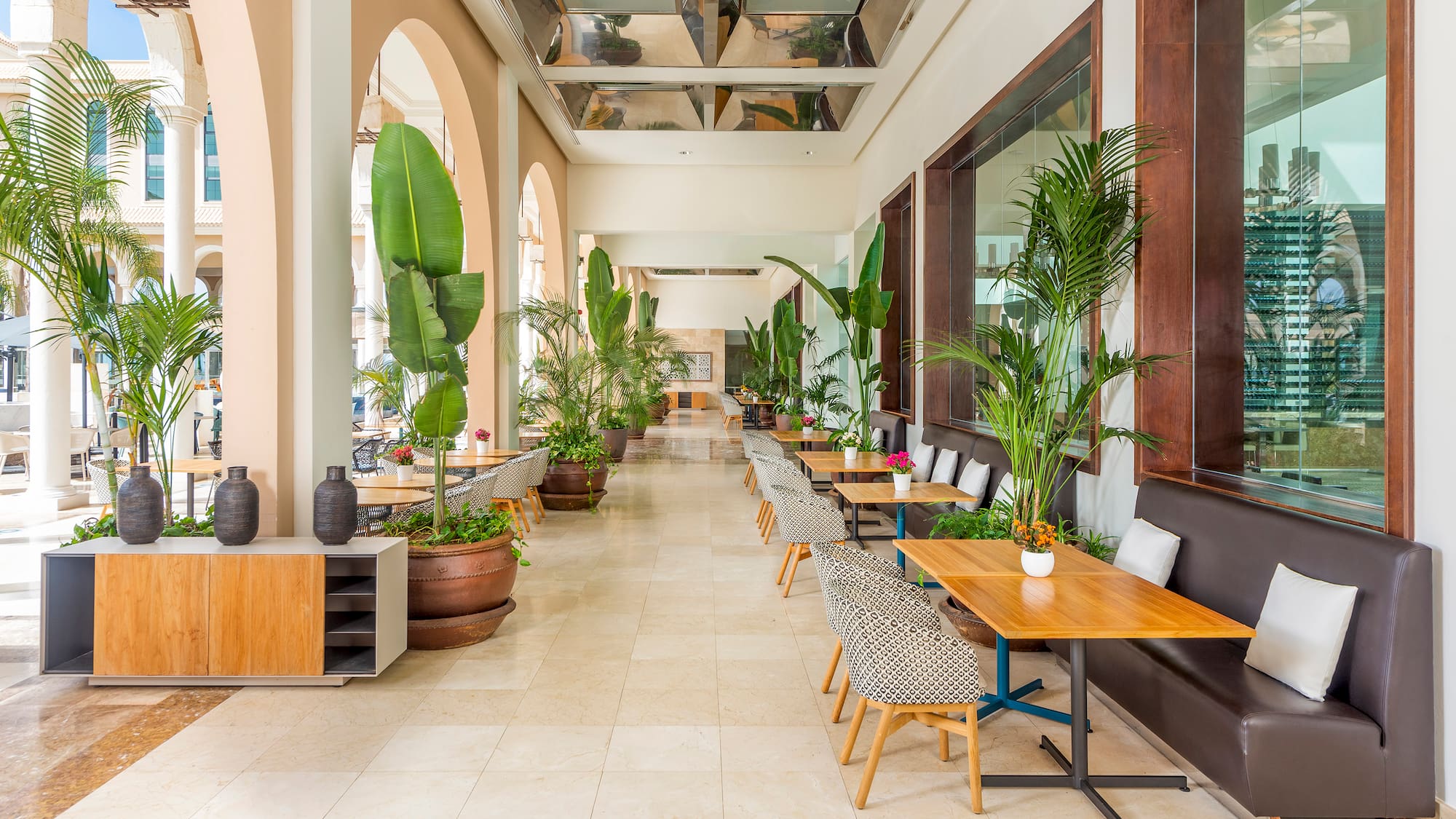 Tropical resort dining area with lush plants, modern tables, and arched architecture.