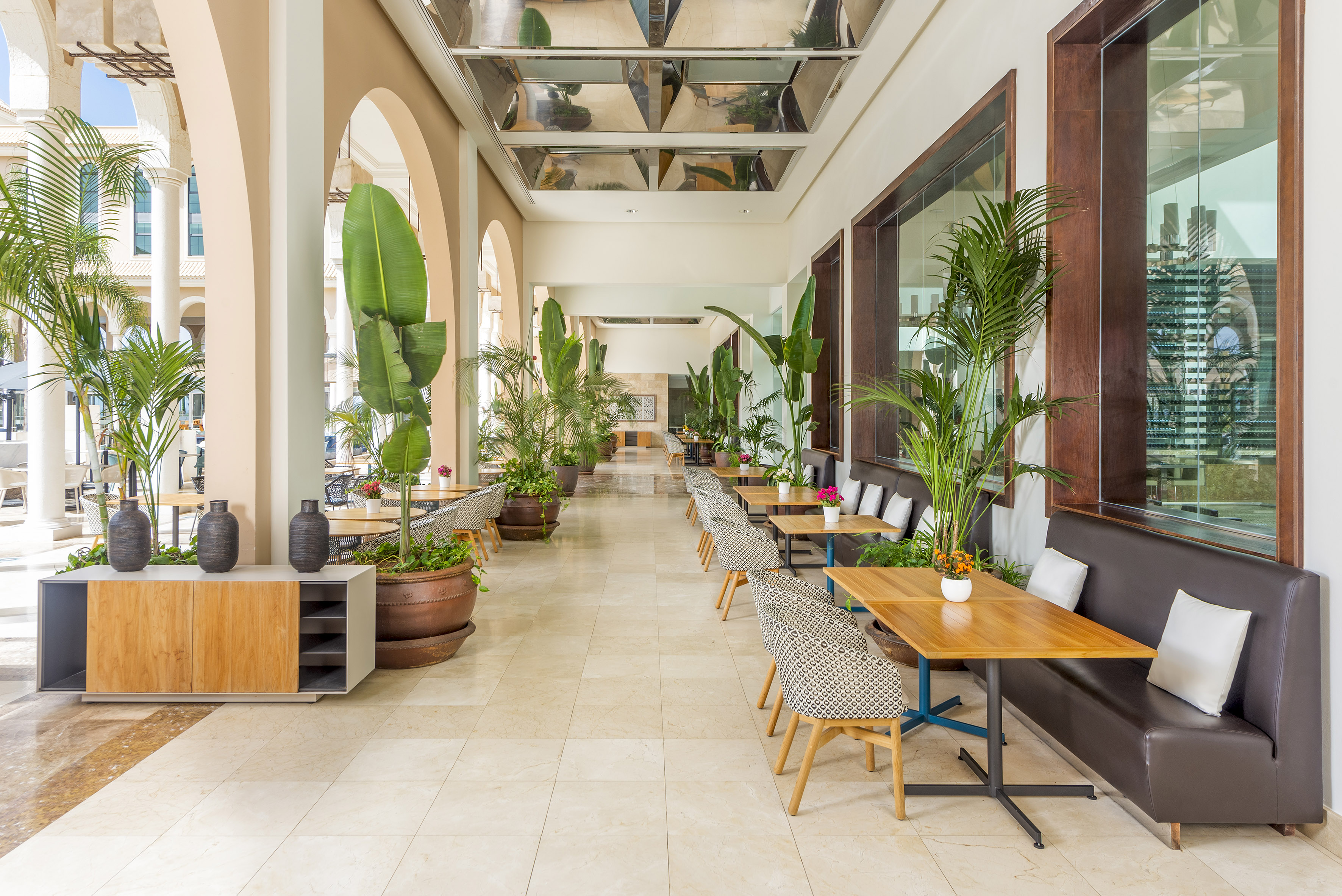 Tropical resort dining area with lush plants, modern tables, and arched architecture.