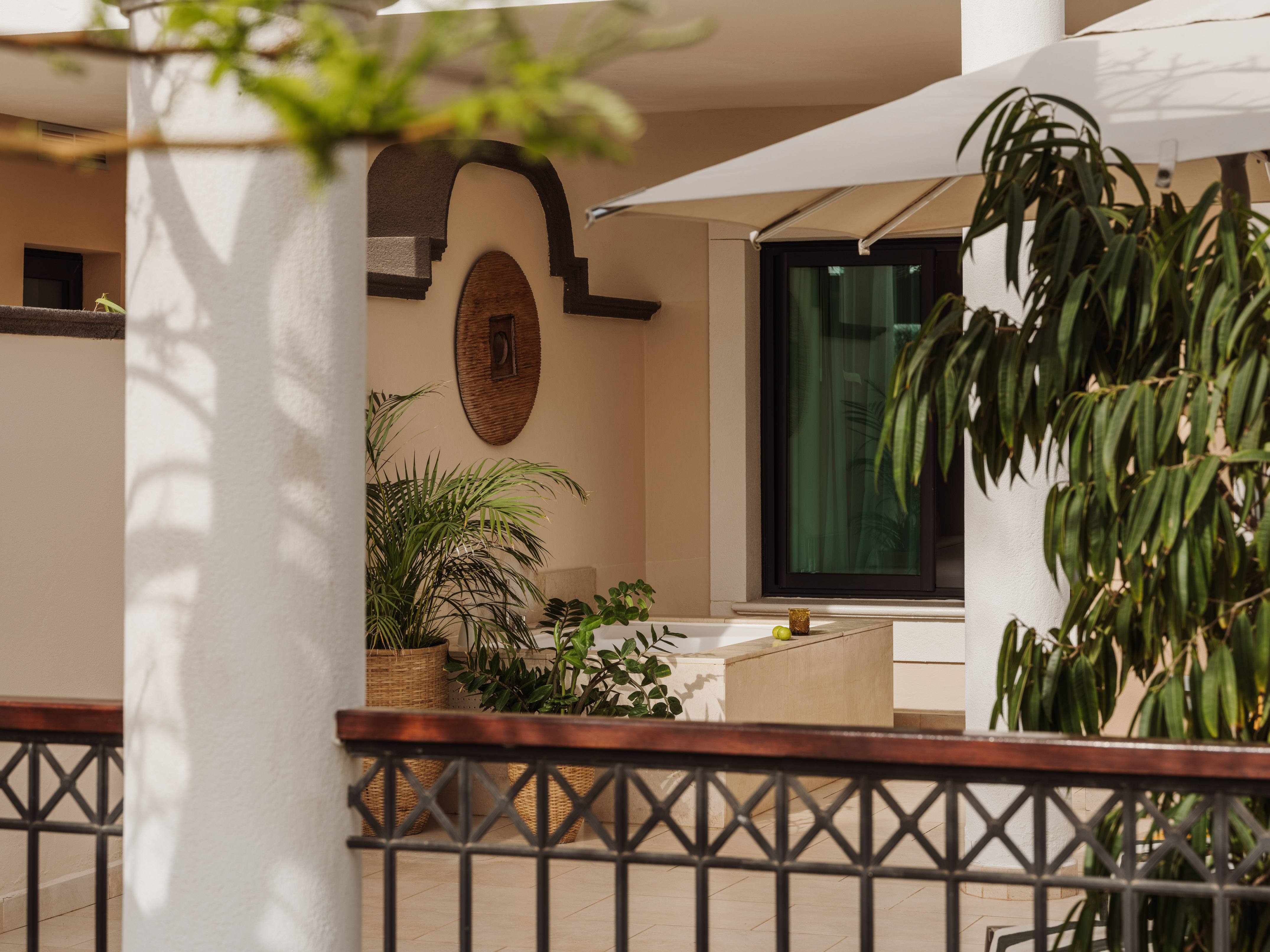 Patio with potted plants, decorative wall art, outdoor tub, and white umbrella.