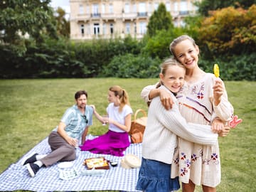 a man and woman sitting on a blanket in a park