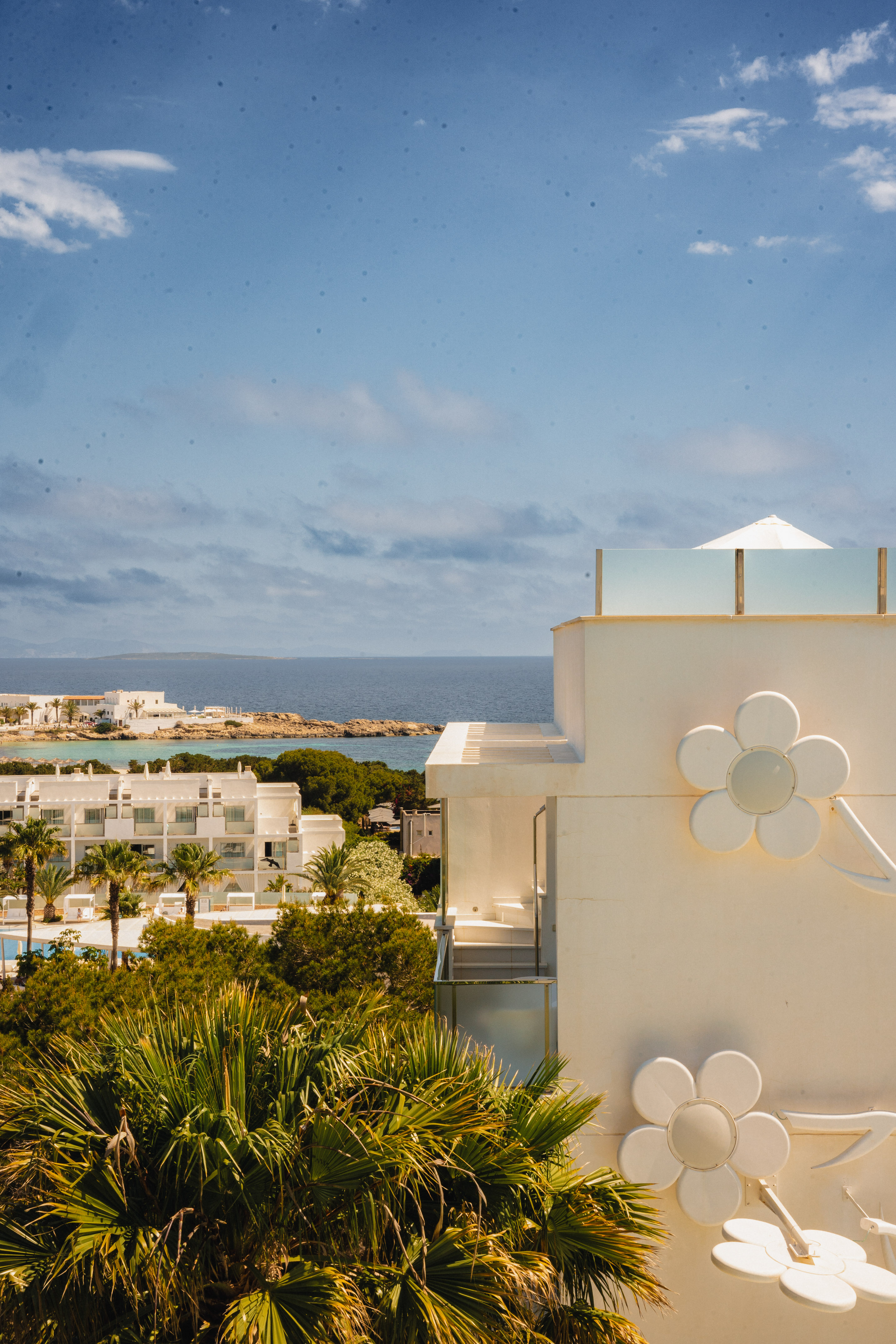 Coastal resort with white buildings, sea view, palm trees, and flower decor.