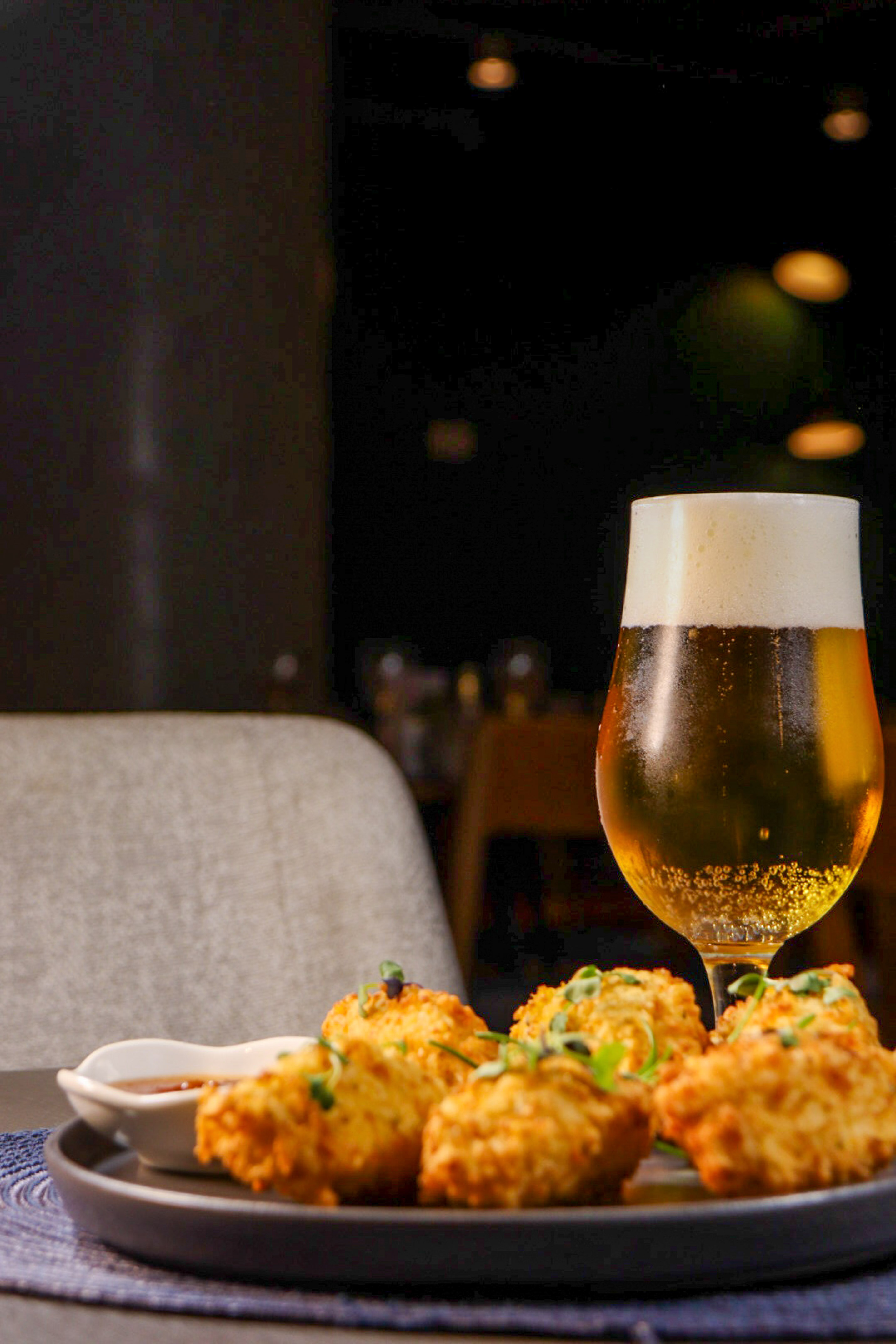 Cerveza rubia y aperitivos fritos con salsa en plato, ambiente de bar.
