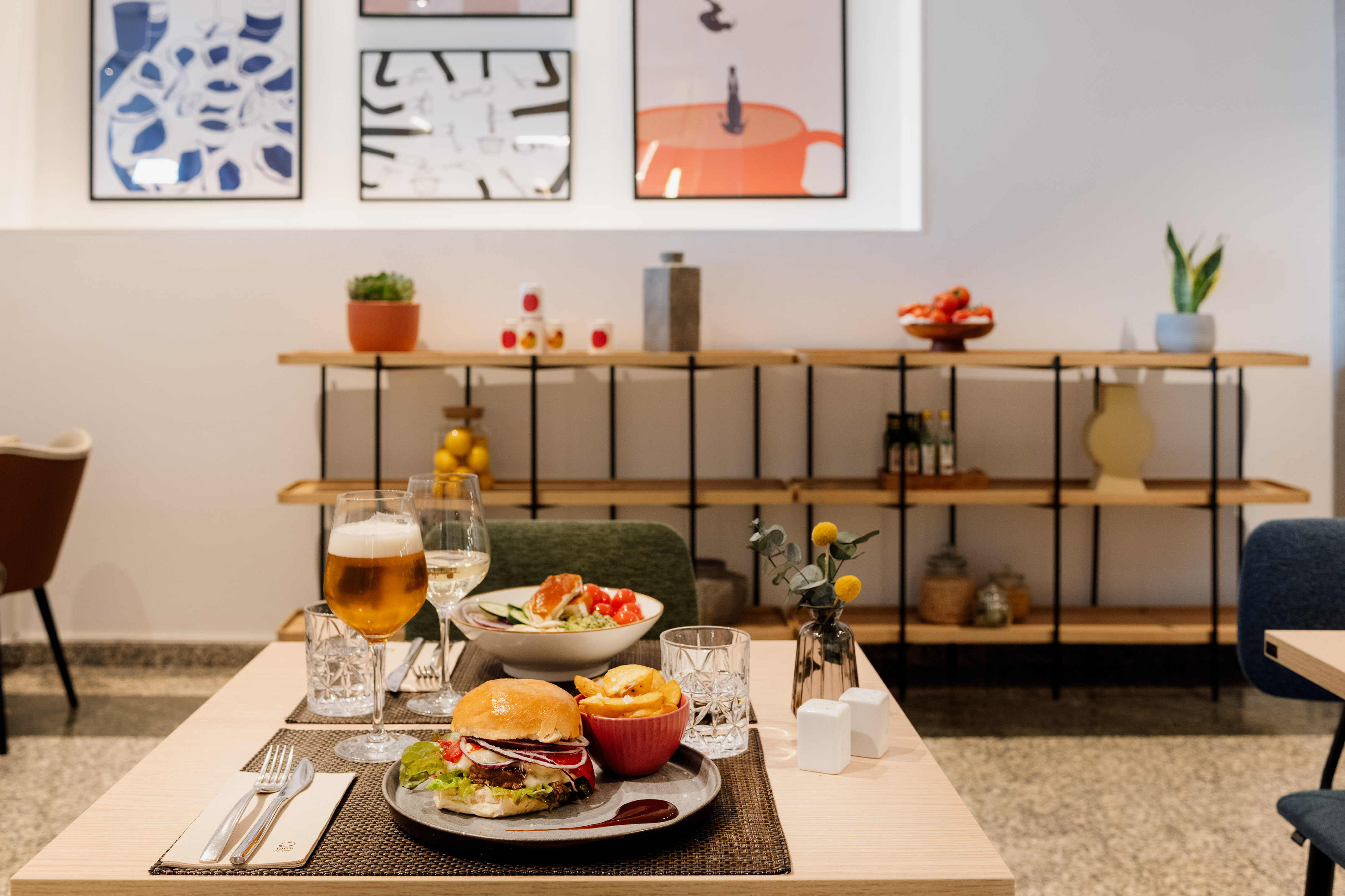 Restaurant table with burger, fries, salad, beer, and wine. Modern dining setting.