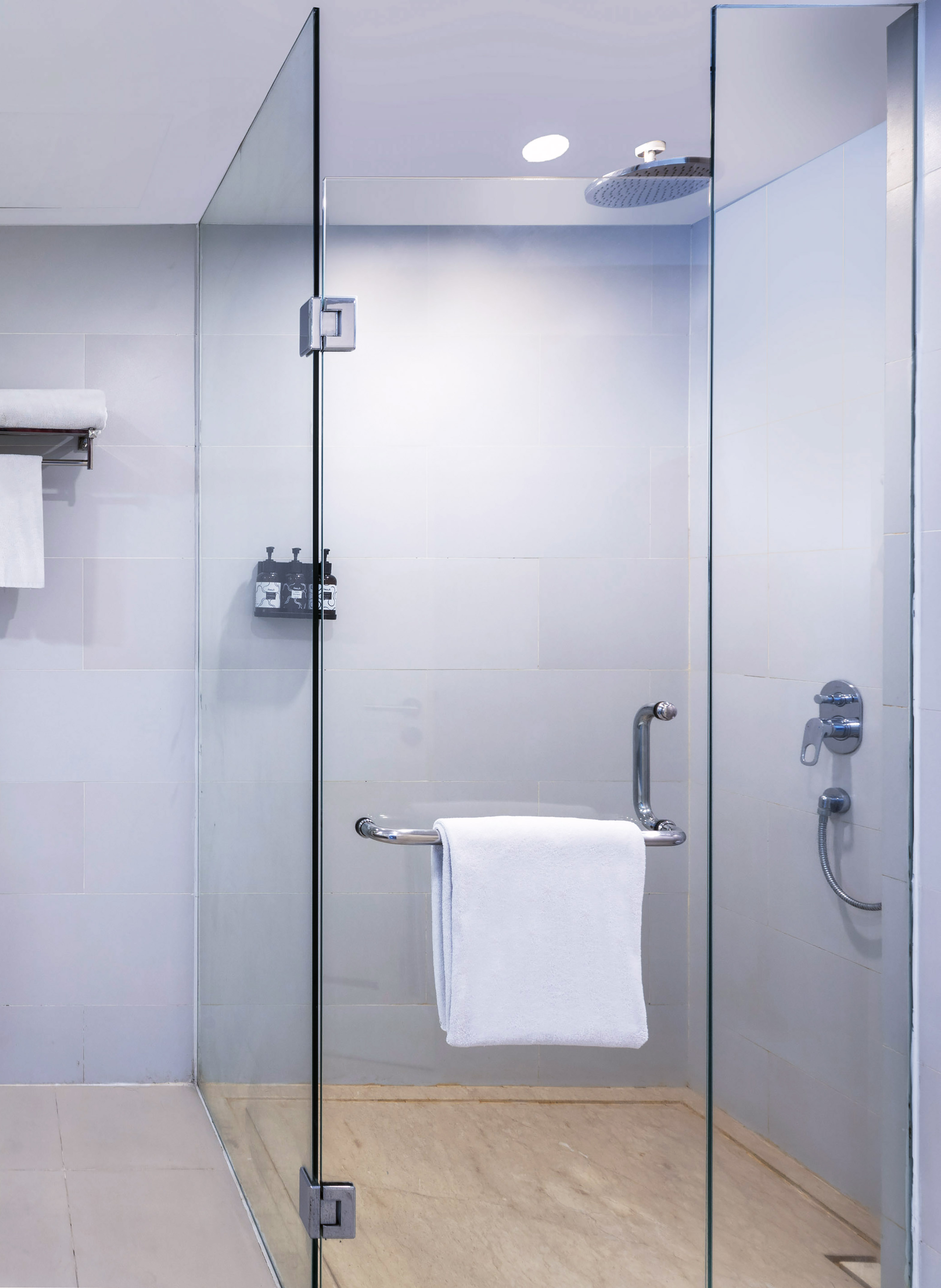 Modern walk-in glass shower with rain head, white towel, and tiled floor.