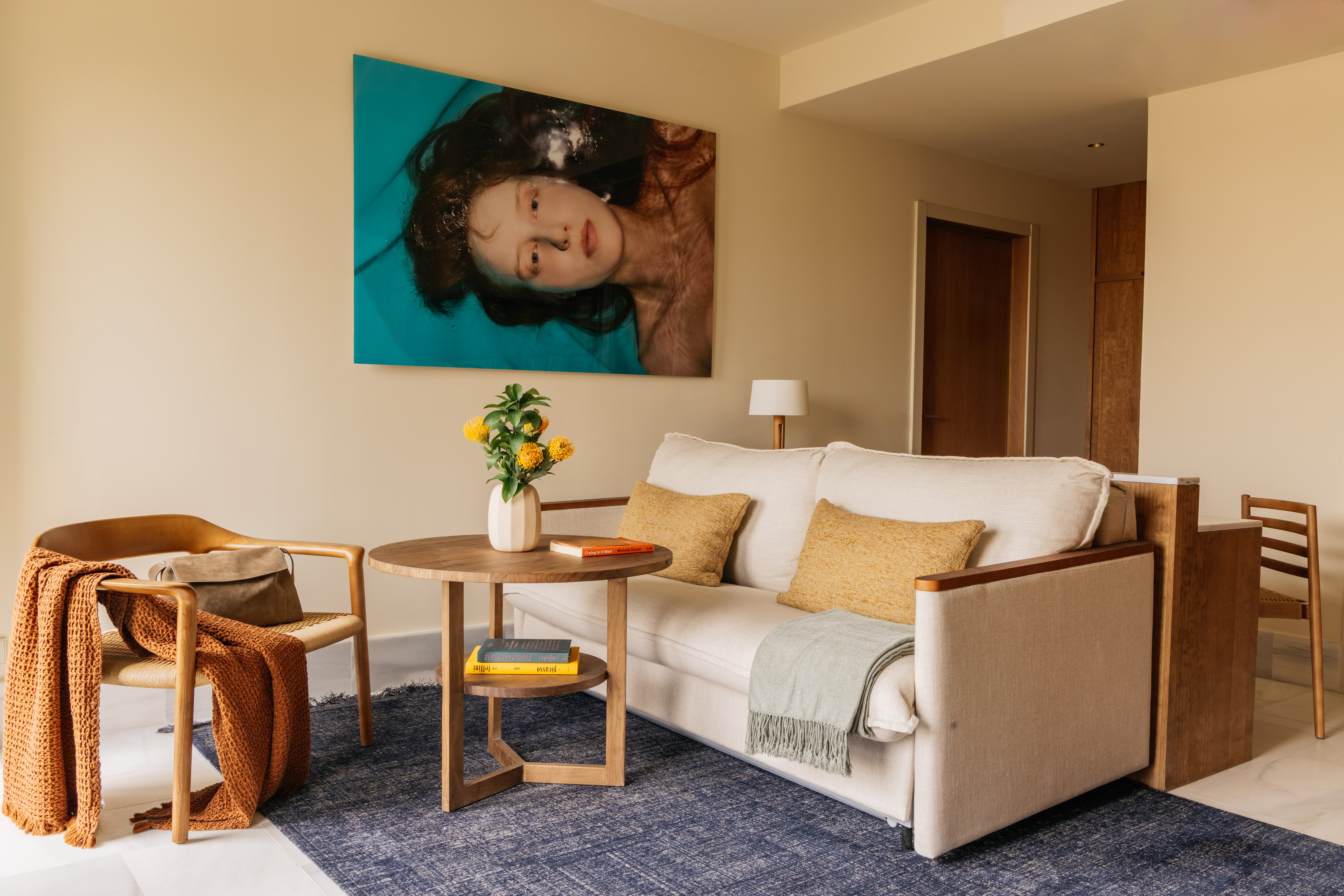 Modern living room: cream sofa, wooden armchair, blue rug, woman in water art.
