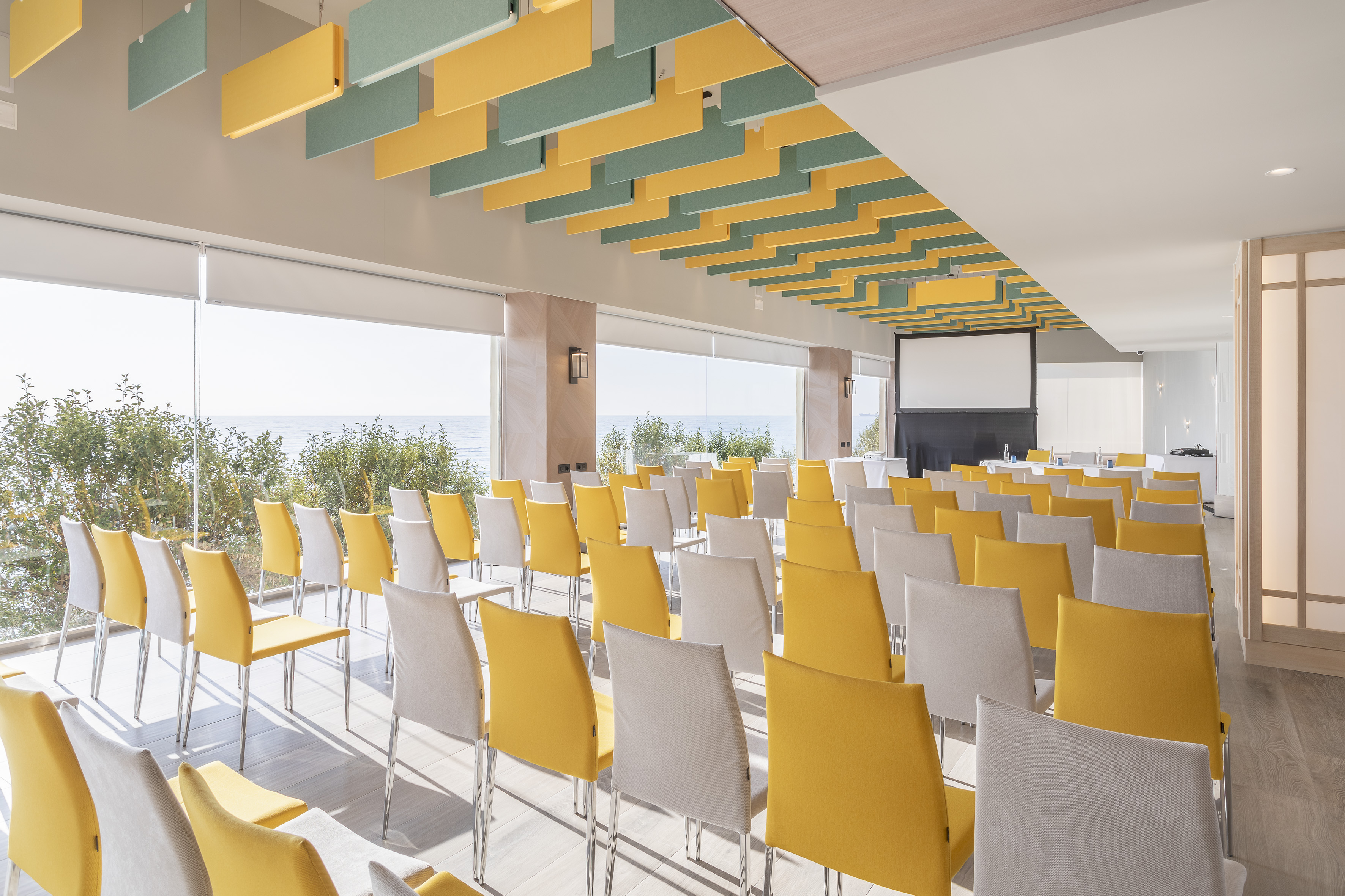 Modern conference room, ocean view, yellow chairs, projector, acoustic ceiling.