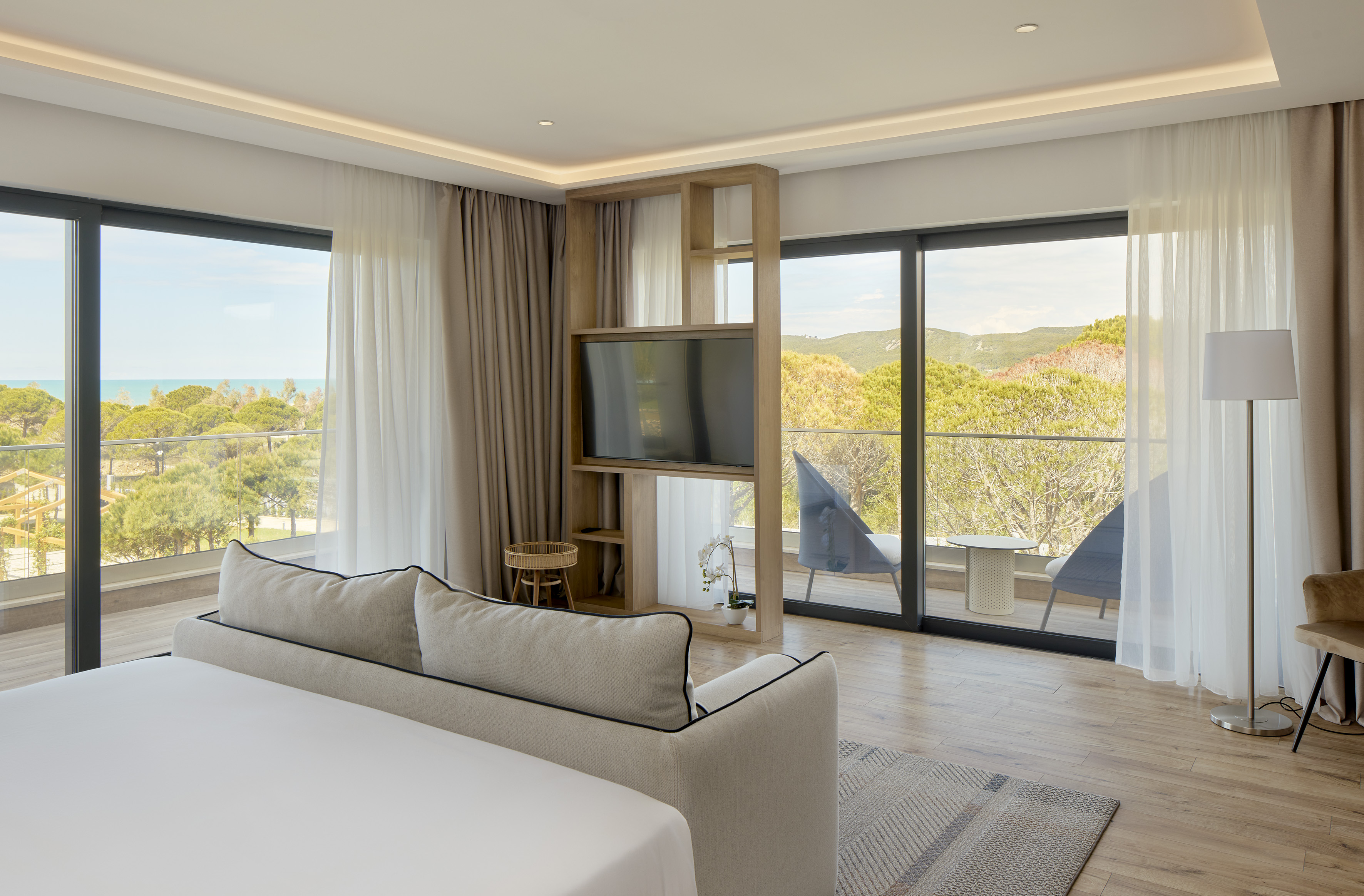 Modern bedroom with sea view balcony, lush green landscape, and comfortable bed.