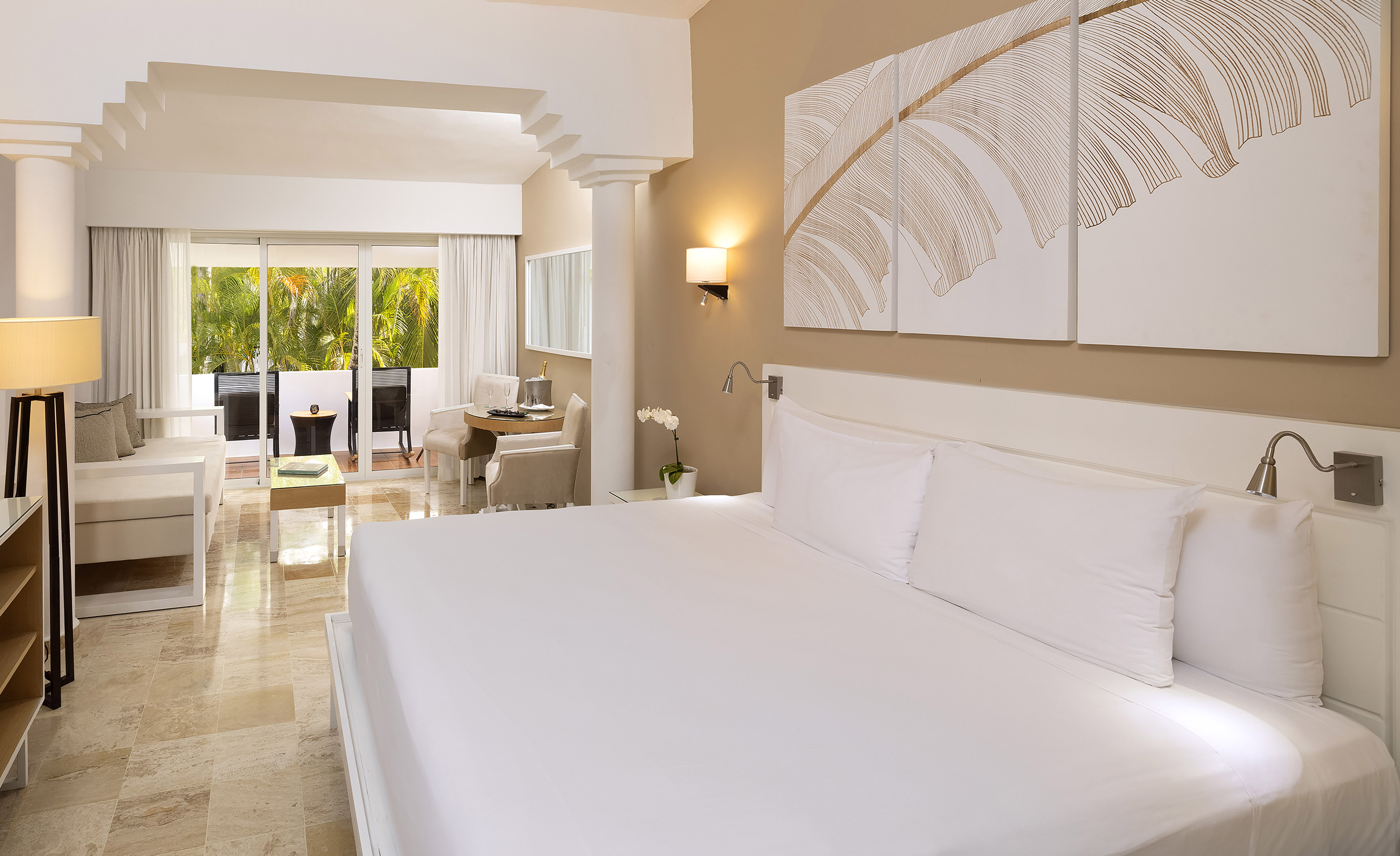Modern hotel suite with king bed, seating area, and tropical balcony view.
