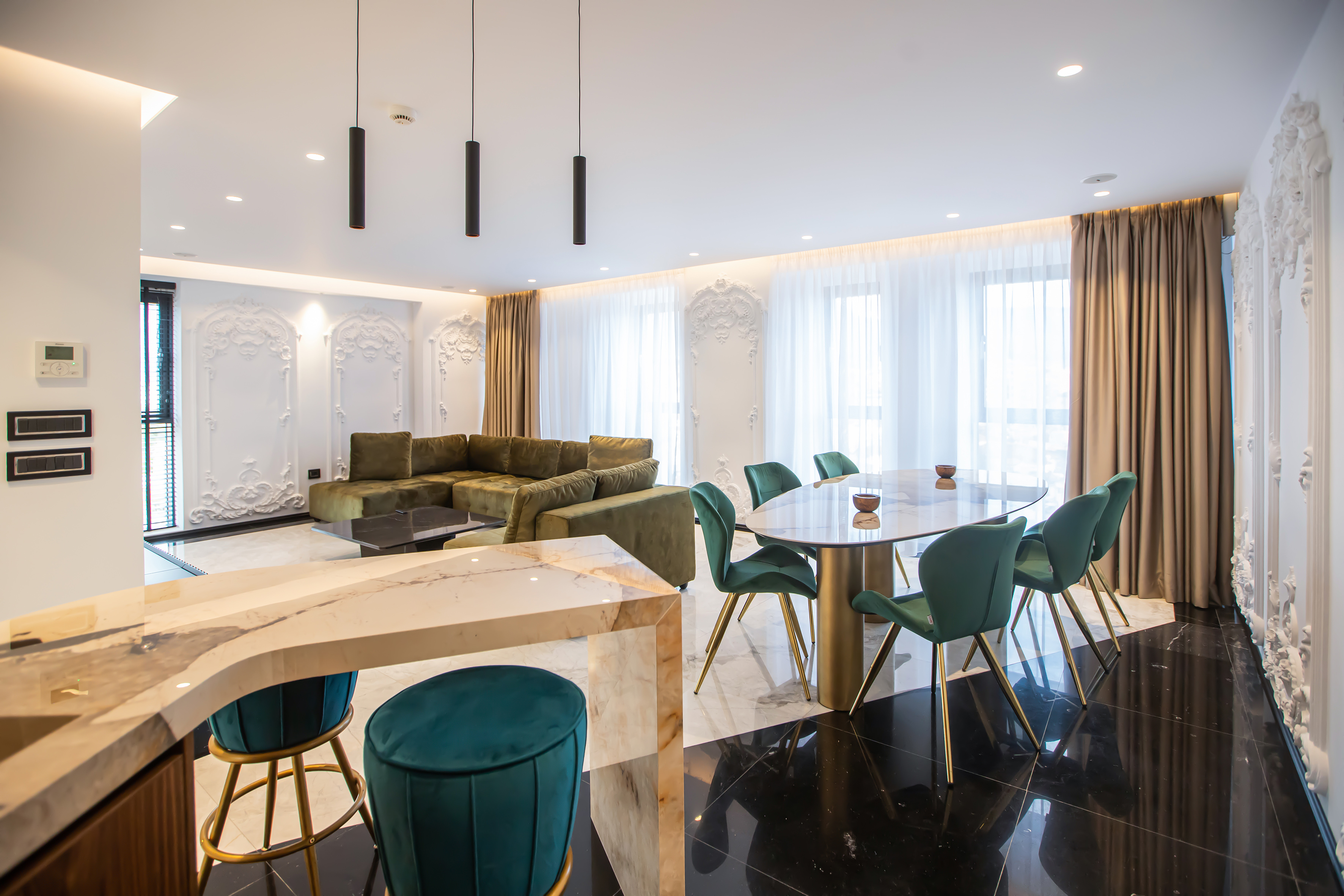 Modern open-plan living room with green sofa, marble dining table, velvet chairs.