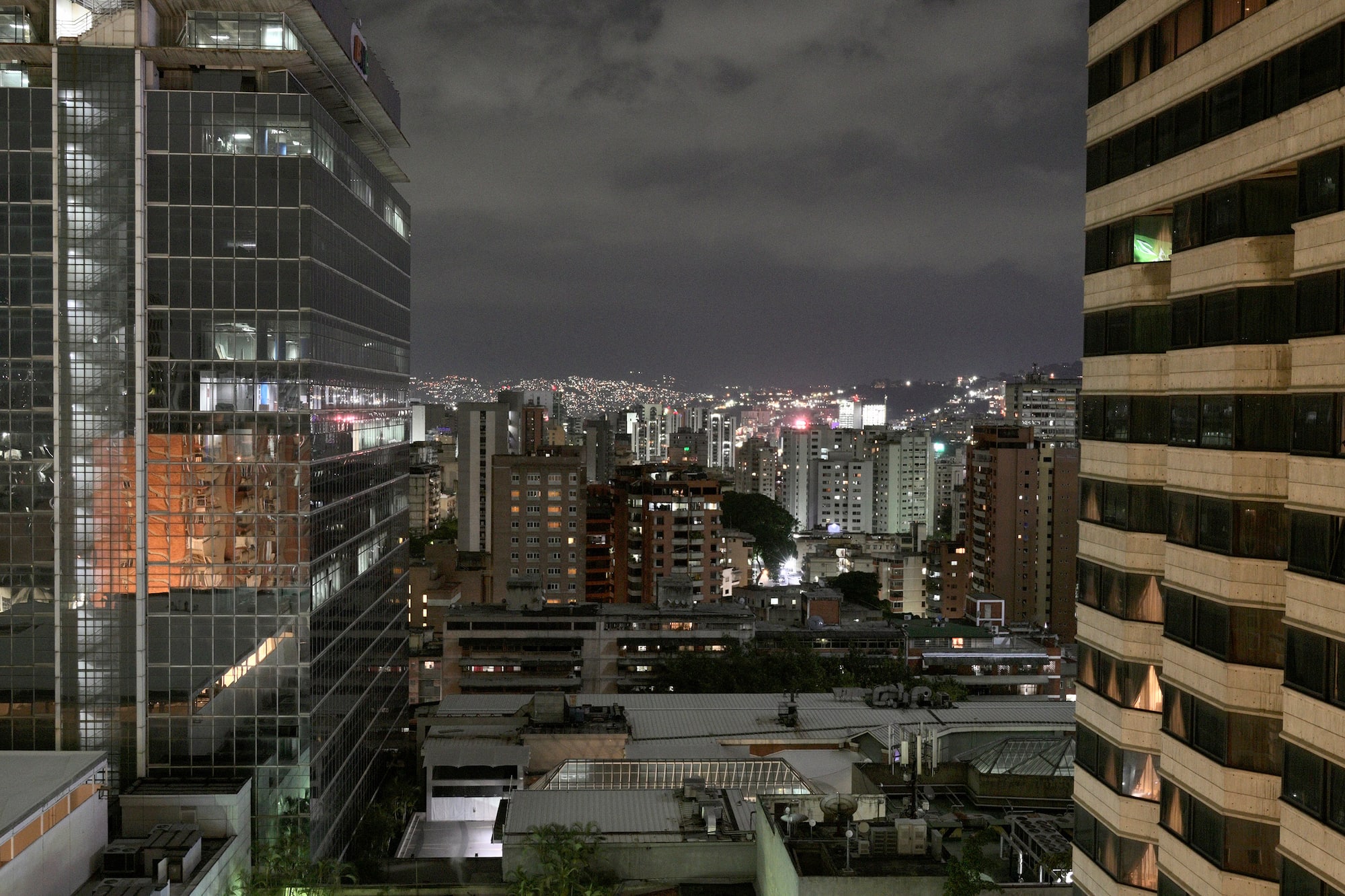 Nighttime Caracas cityscape: BNC building, glowing hotel pool, urban lights.