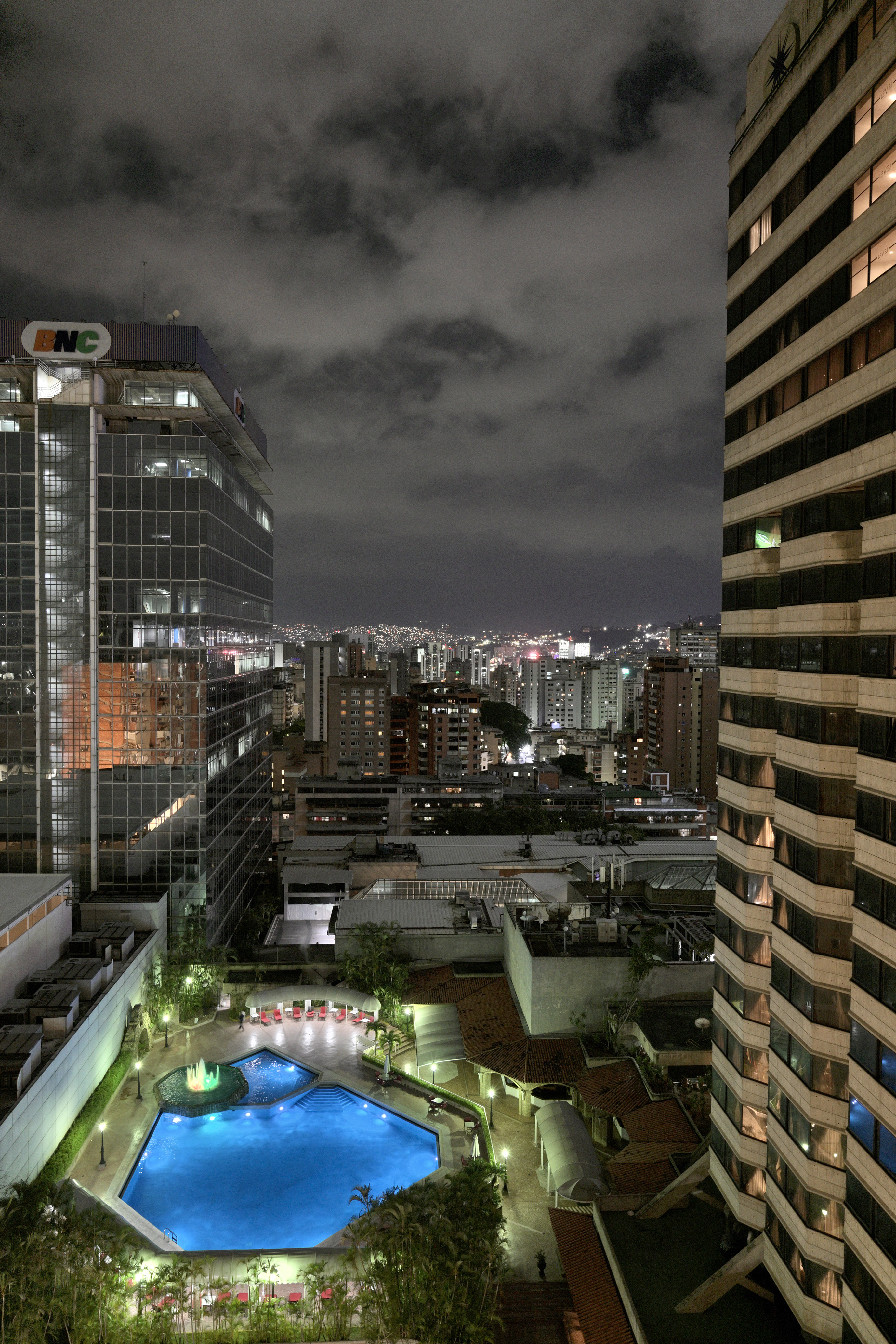 Nighttime Caracas cityscape: BNC building, glowing hotel pool, urban lights.