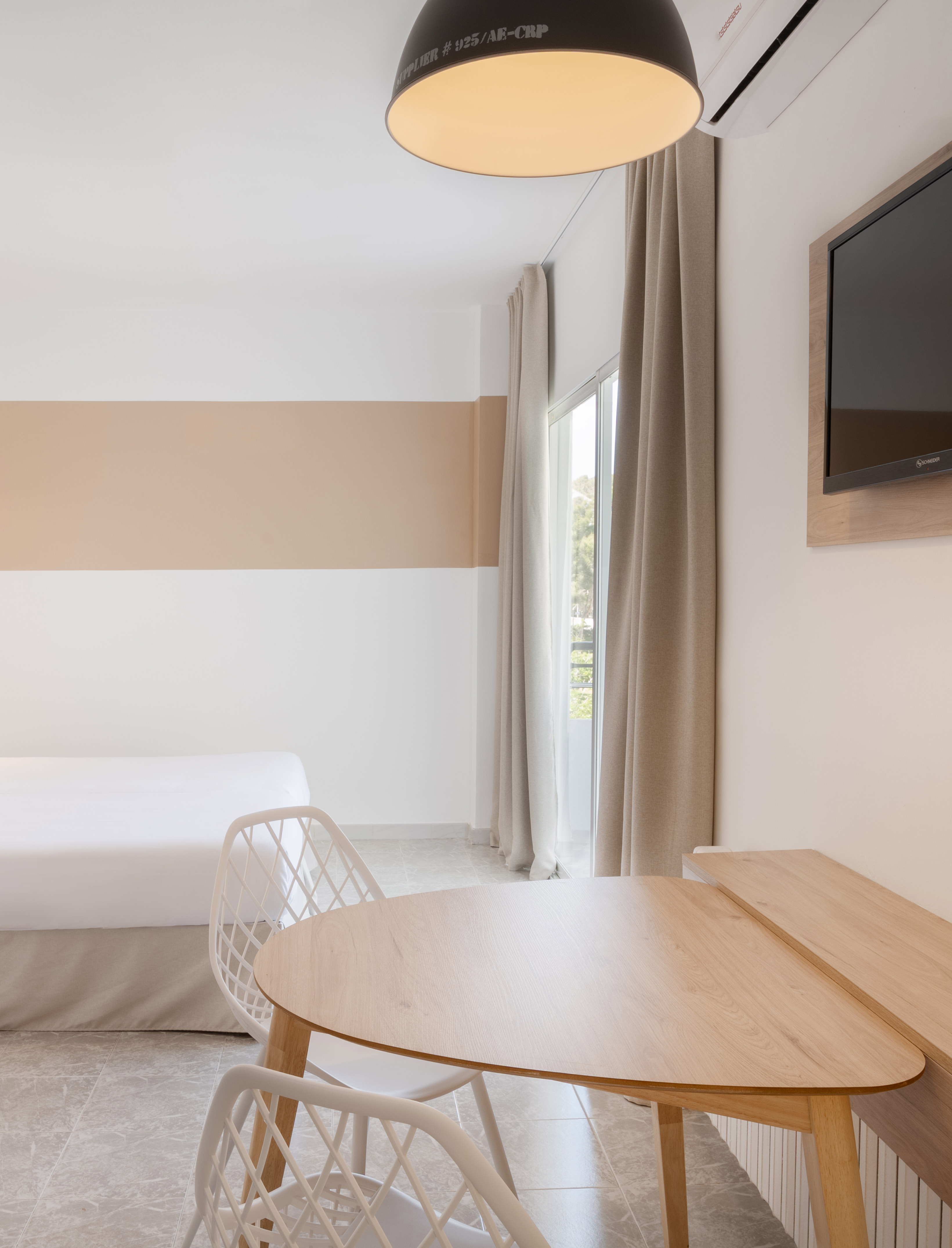 Modern hotel room with bed, wood dining table, white chairs, and TV.