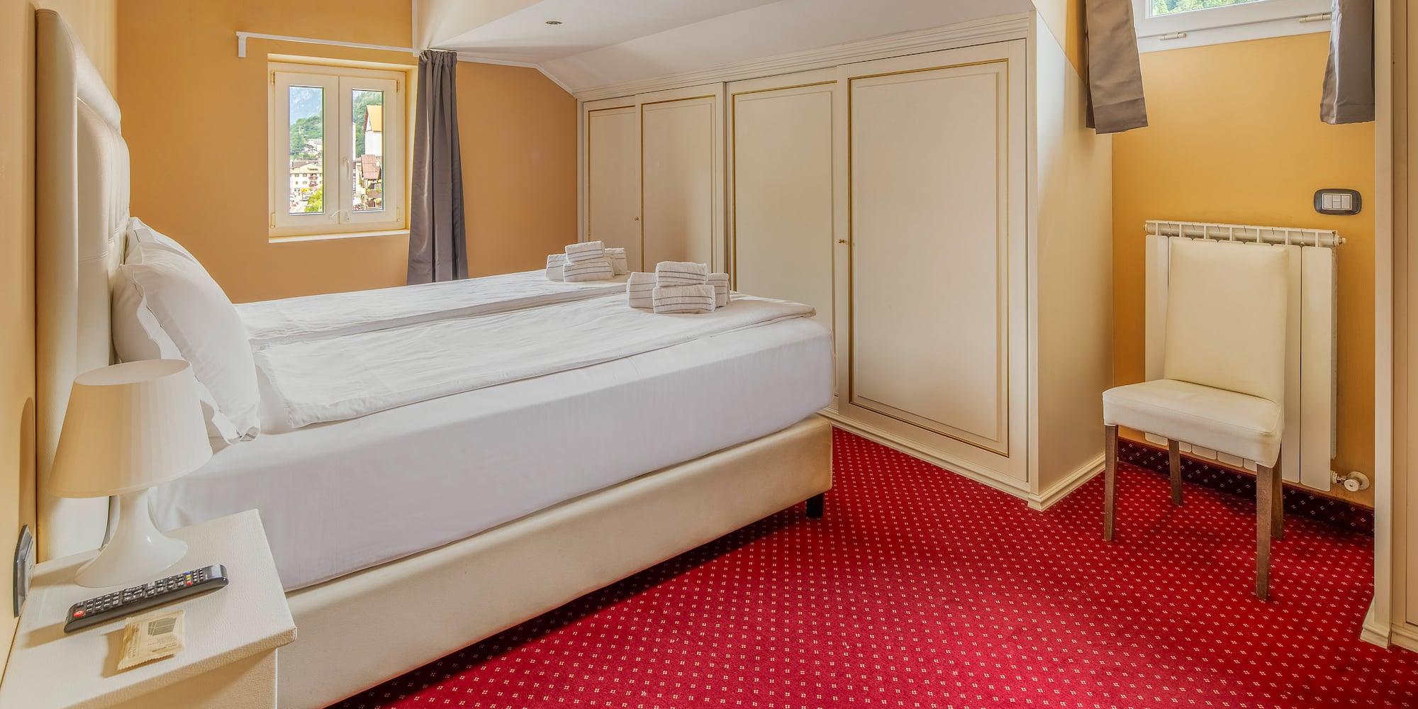 Hotel room with white bed, red carpet, mountain view window, and wardrobes.