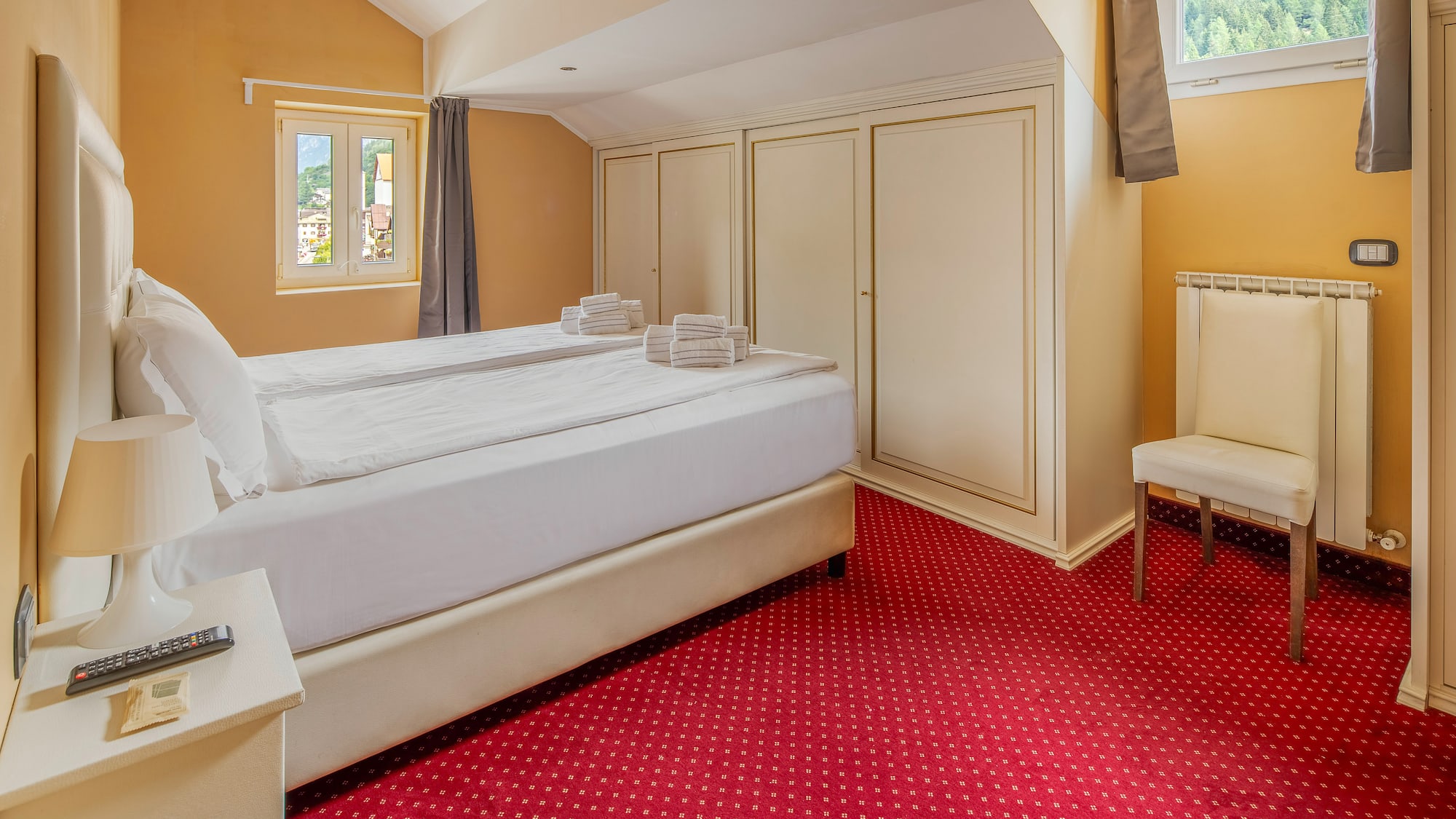 Hotel room with white bed, red carpet, mountain view window, and wardrobes.
