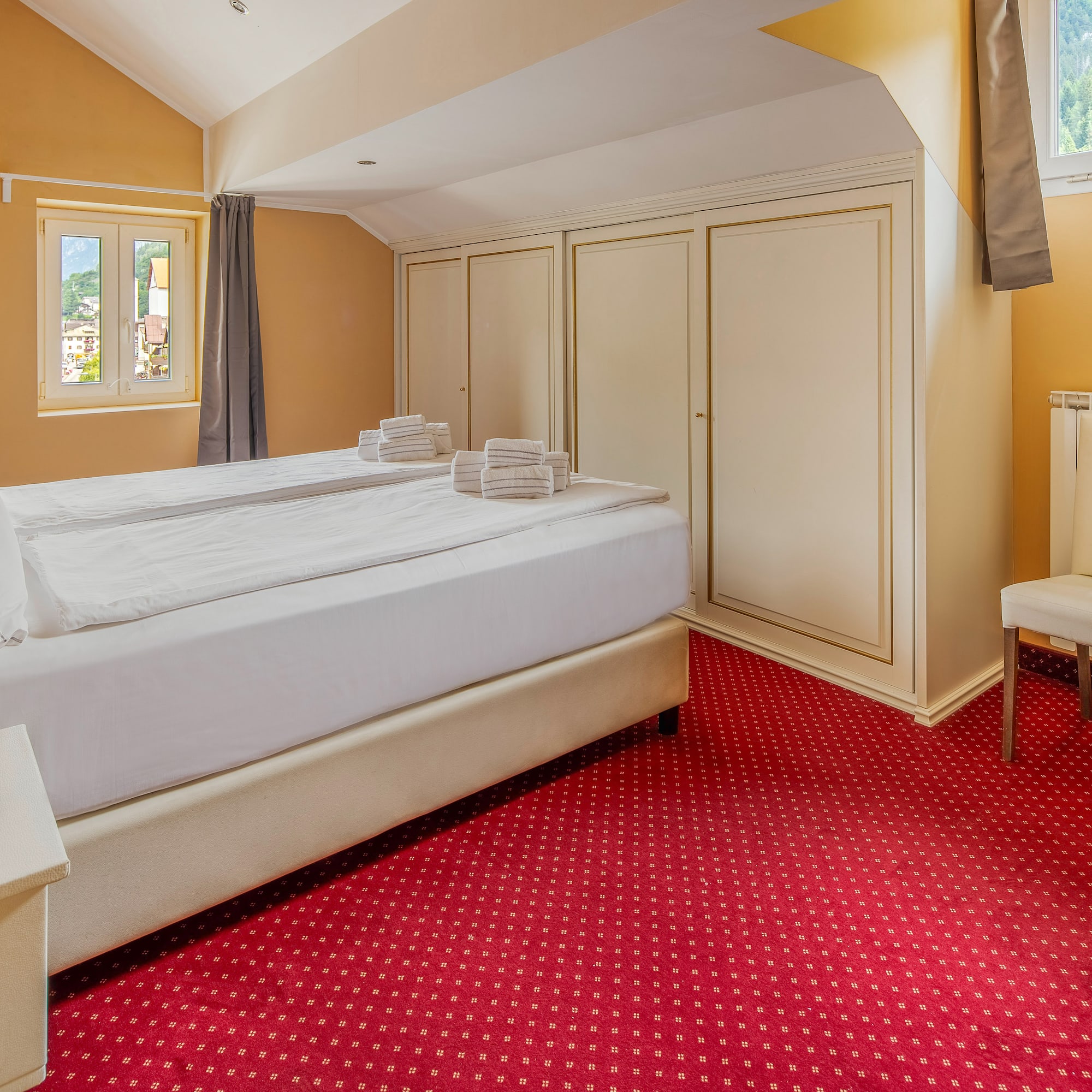 Hotel room with white bed, red carpet, mountain view window, and wardrobes.