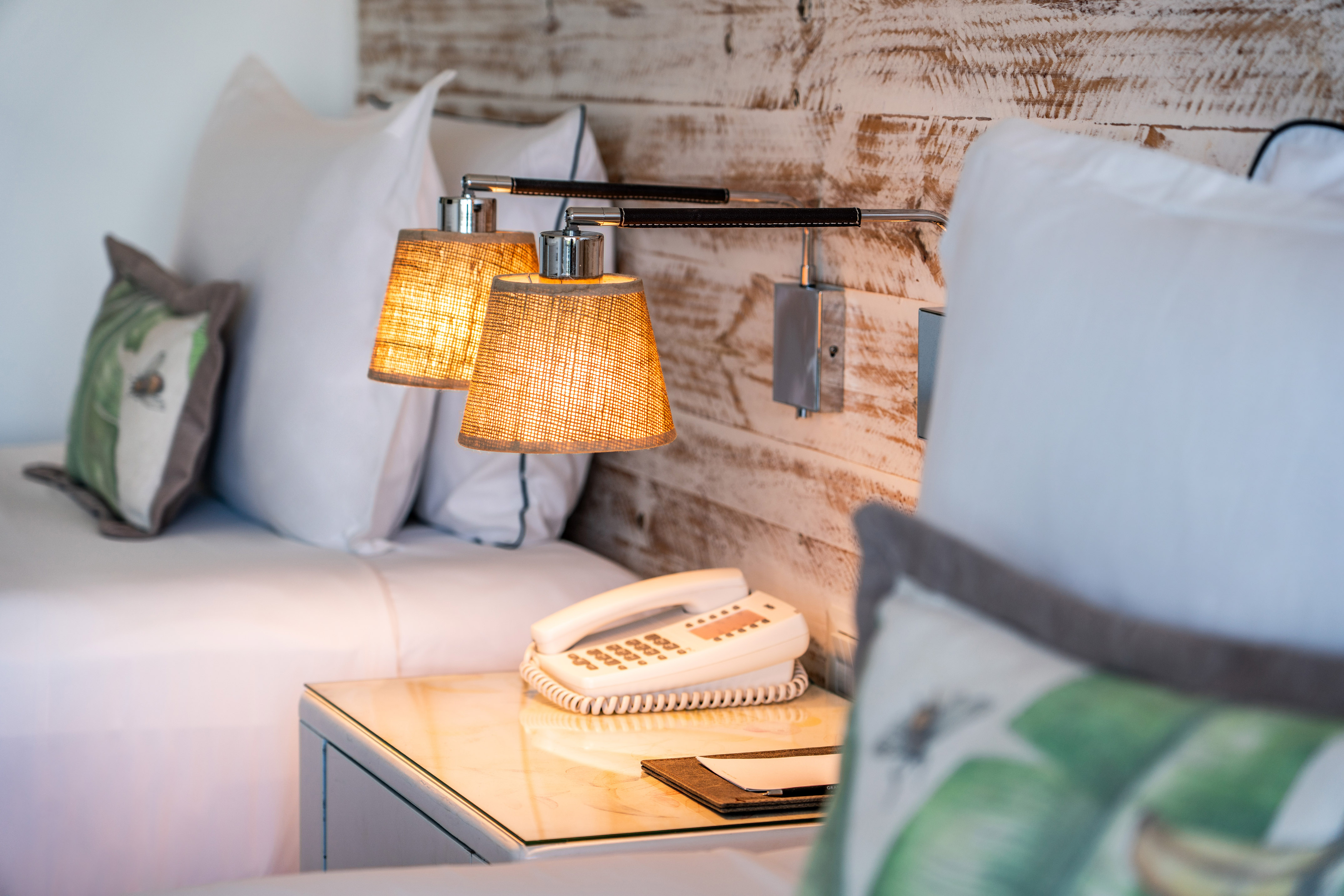 Hotel room with glowing bedside lamps, nightstand, twin beds, and wood panel wall.