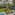 Tropical garden with palm trees, ocean, sun loungers, thatched cabanas, and pool.