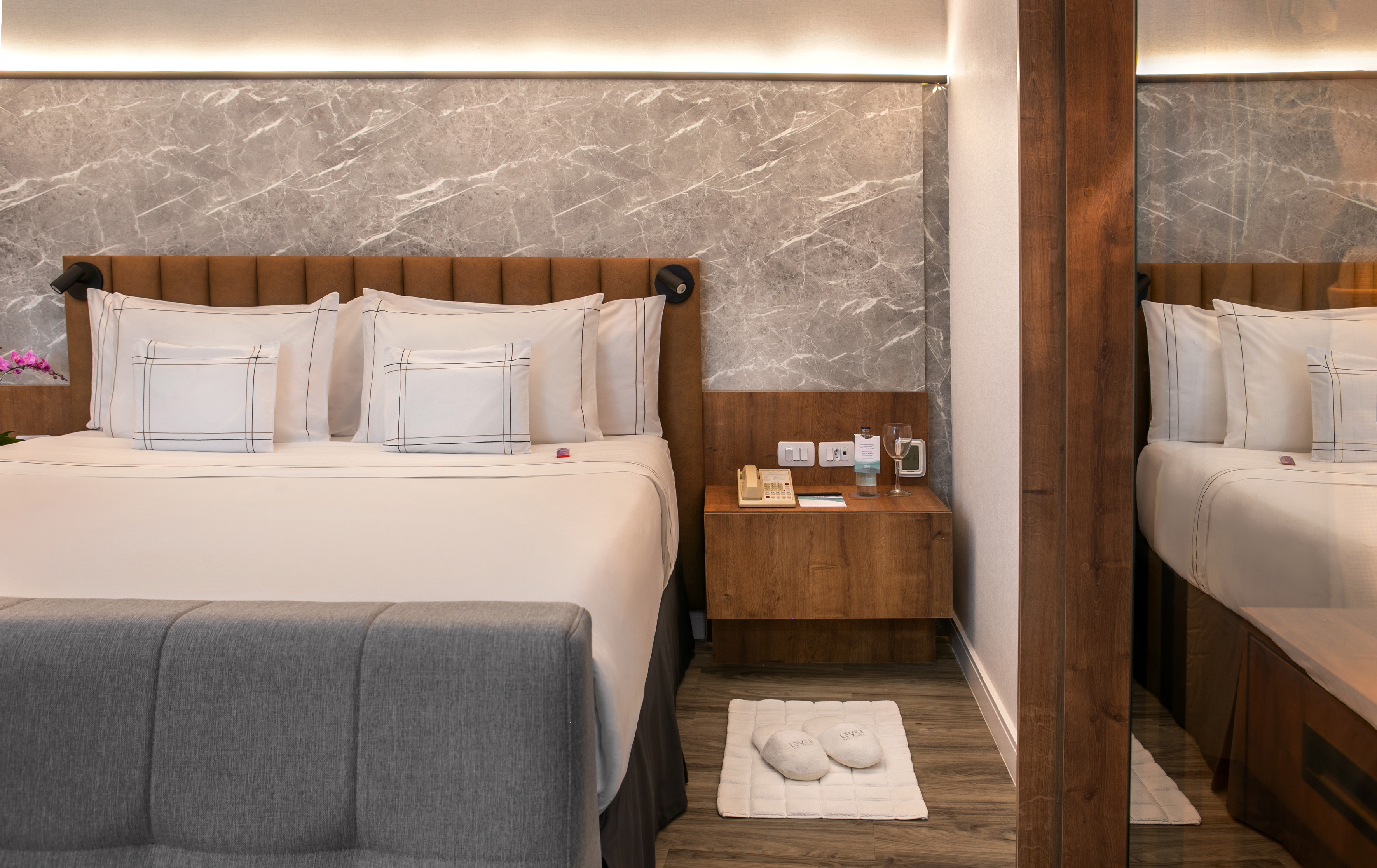 Modern hotel bedroom with large bed, marble accent wall, and wooden nightstand.