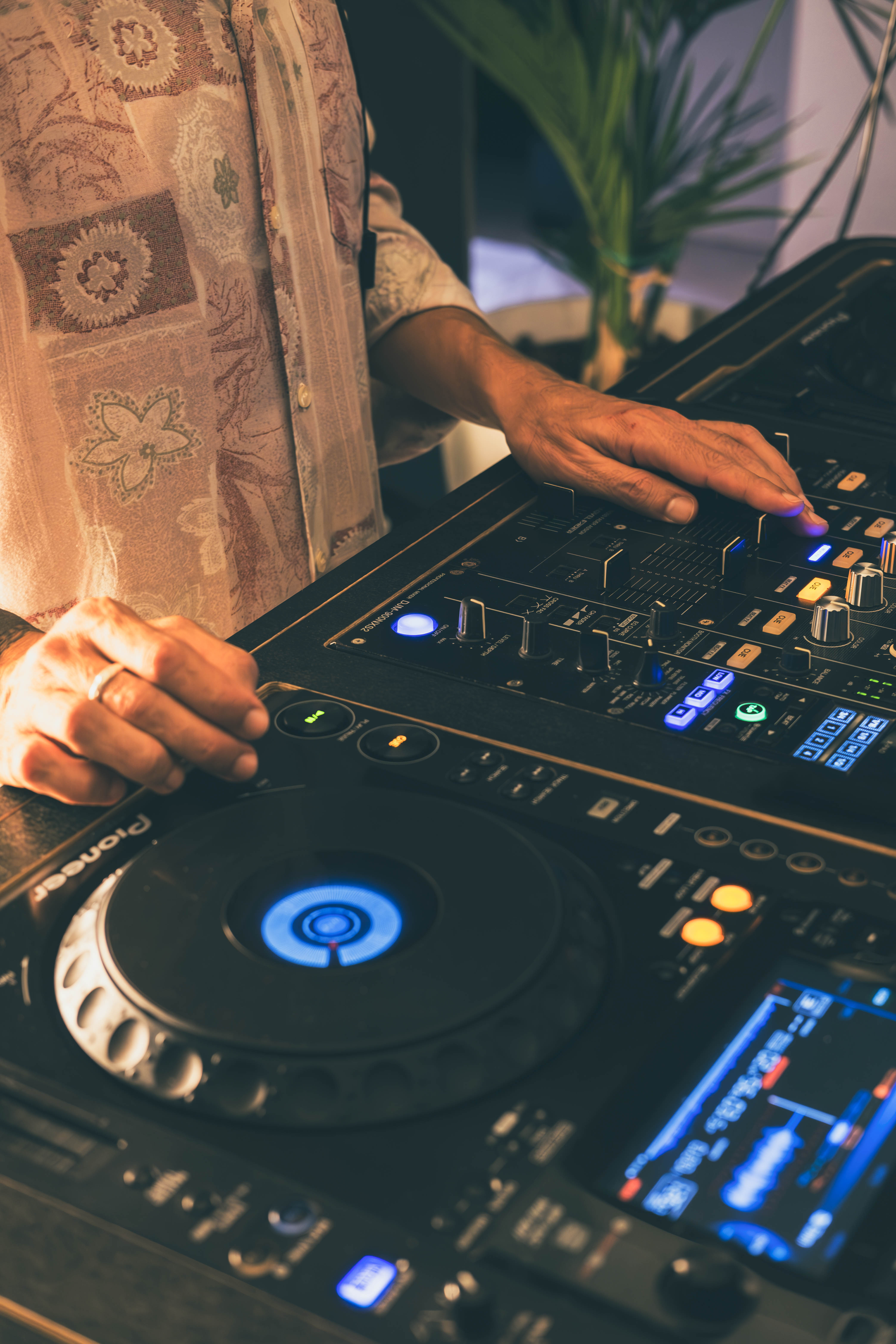 DJ's hands mixing music on a Pioneer mixer with illuminated controls.