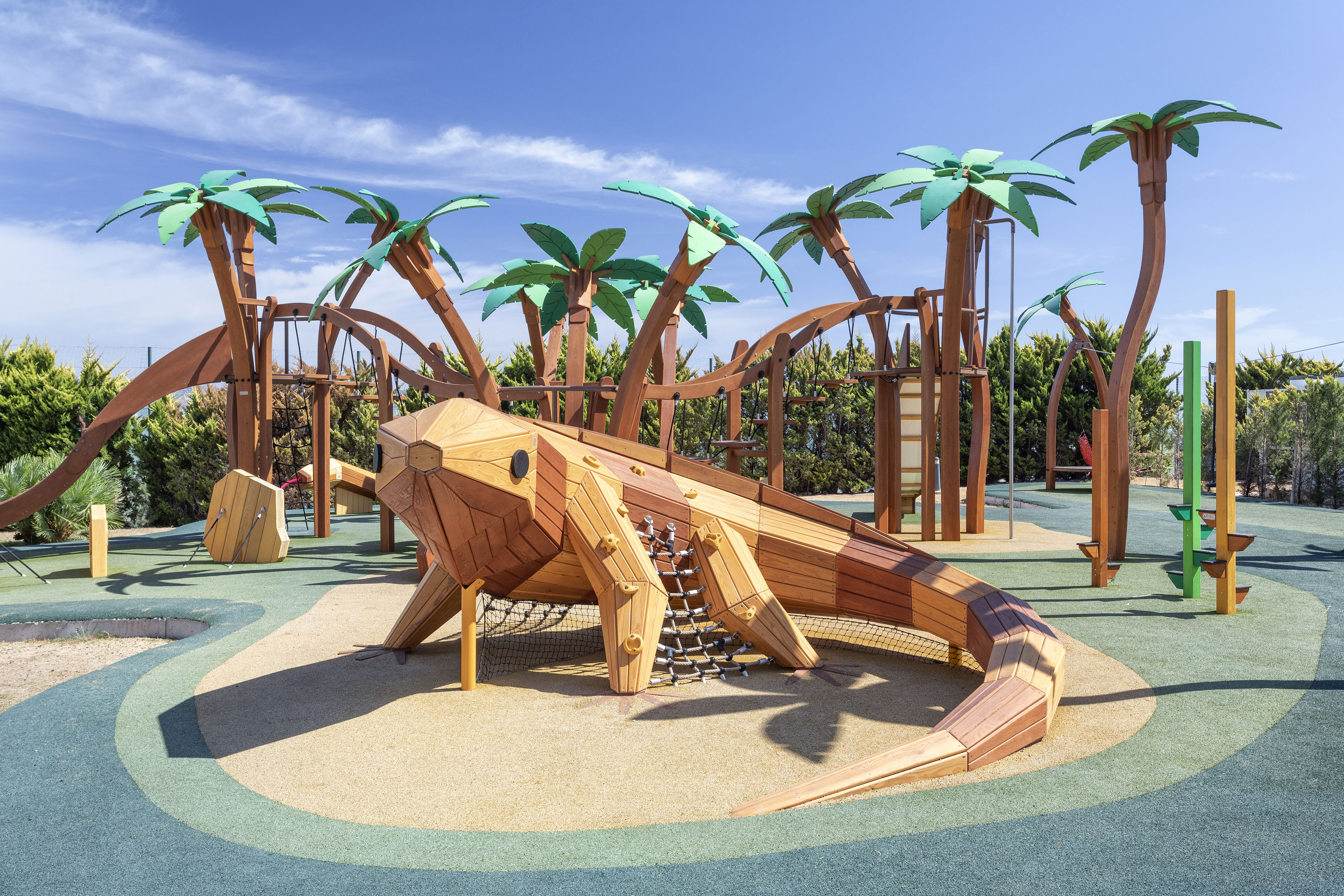 Kids outdoor playground with large wooden lizard and palm tree structures.