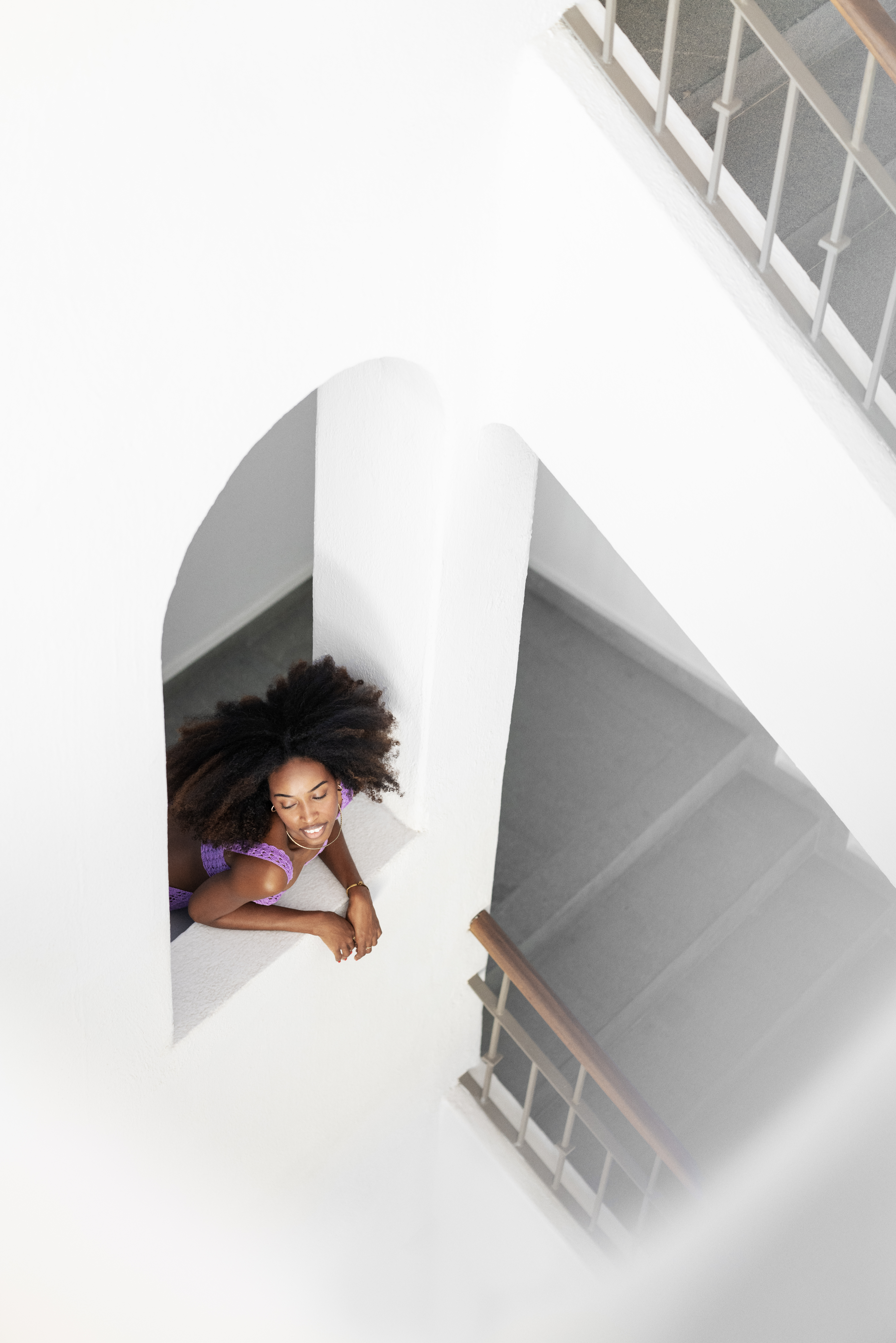 African American woman with curly hair in purple top on white architectural ledge.