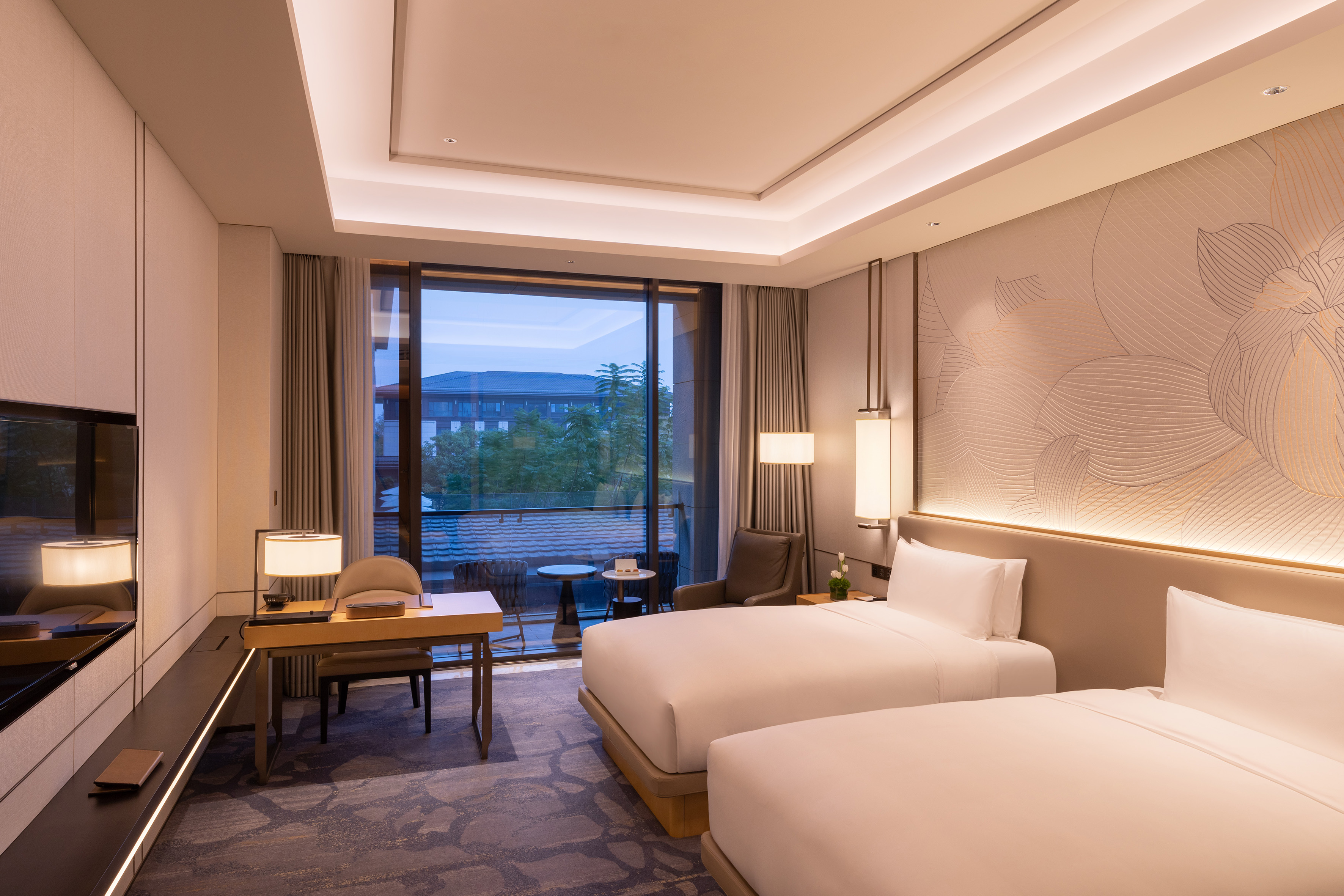 Modern hotel room with two twin beds, desk area, and a large balcony.