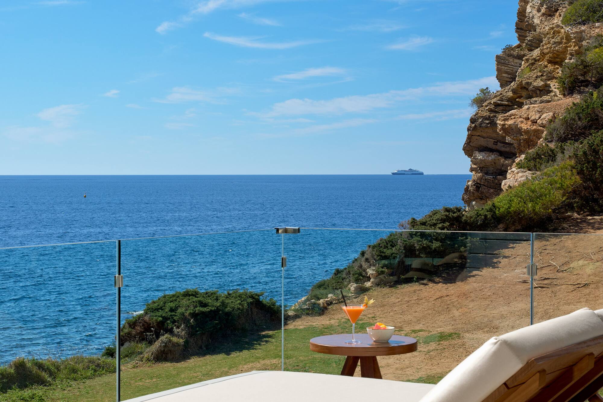 Luxury ocean view balcony with sun lounger, cocktail, and cliff.