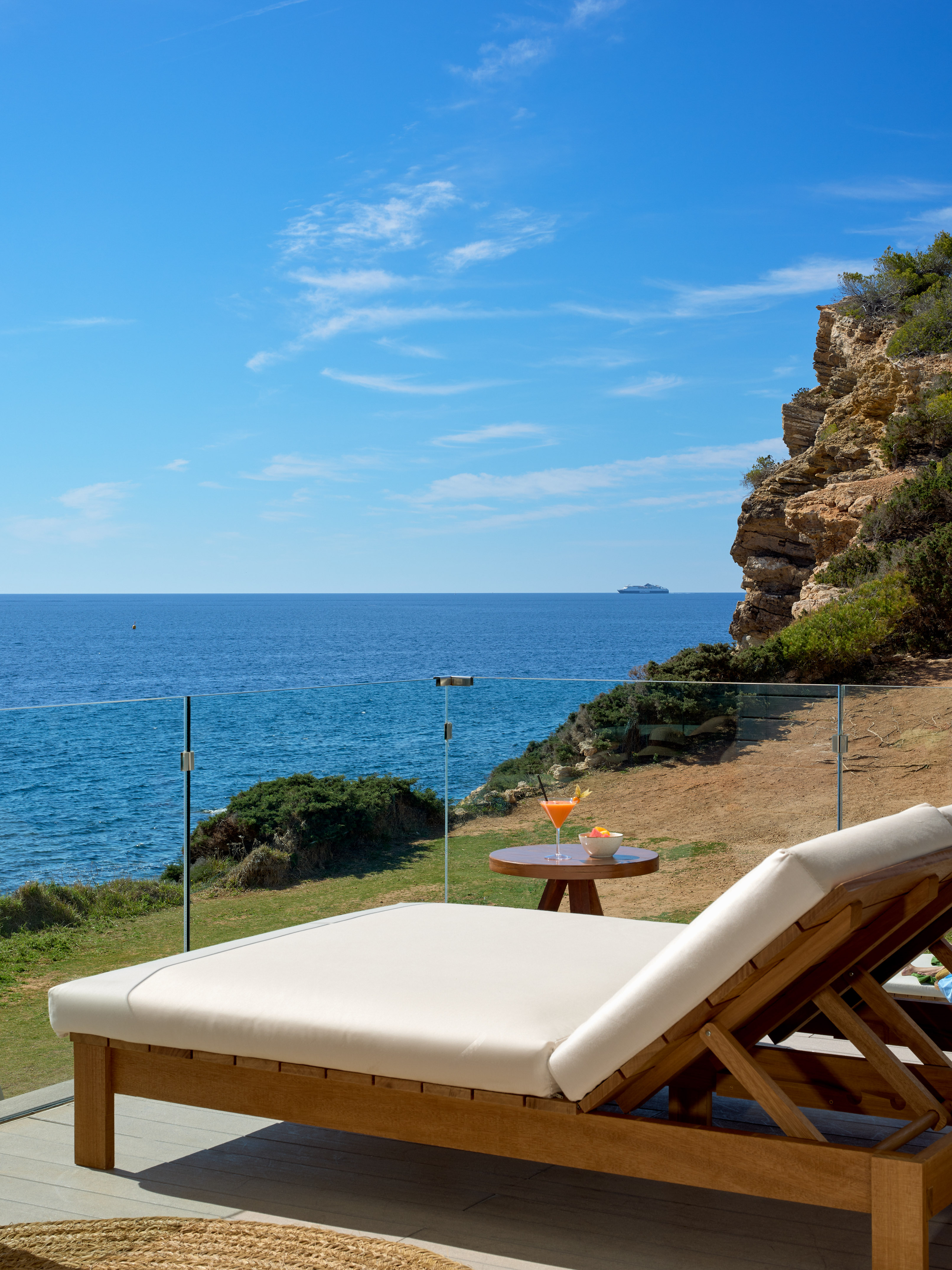 Luxury ocean view balcony with sun lounger, cocktail, and cliff.