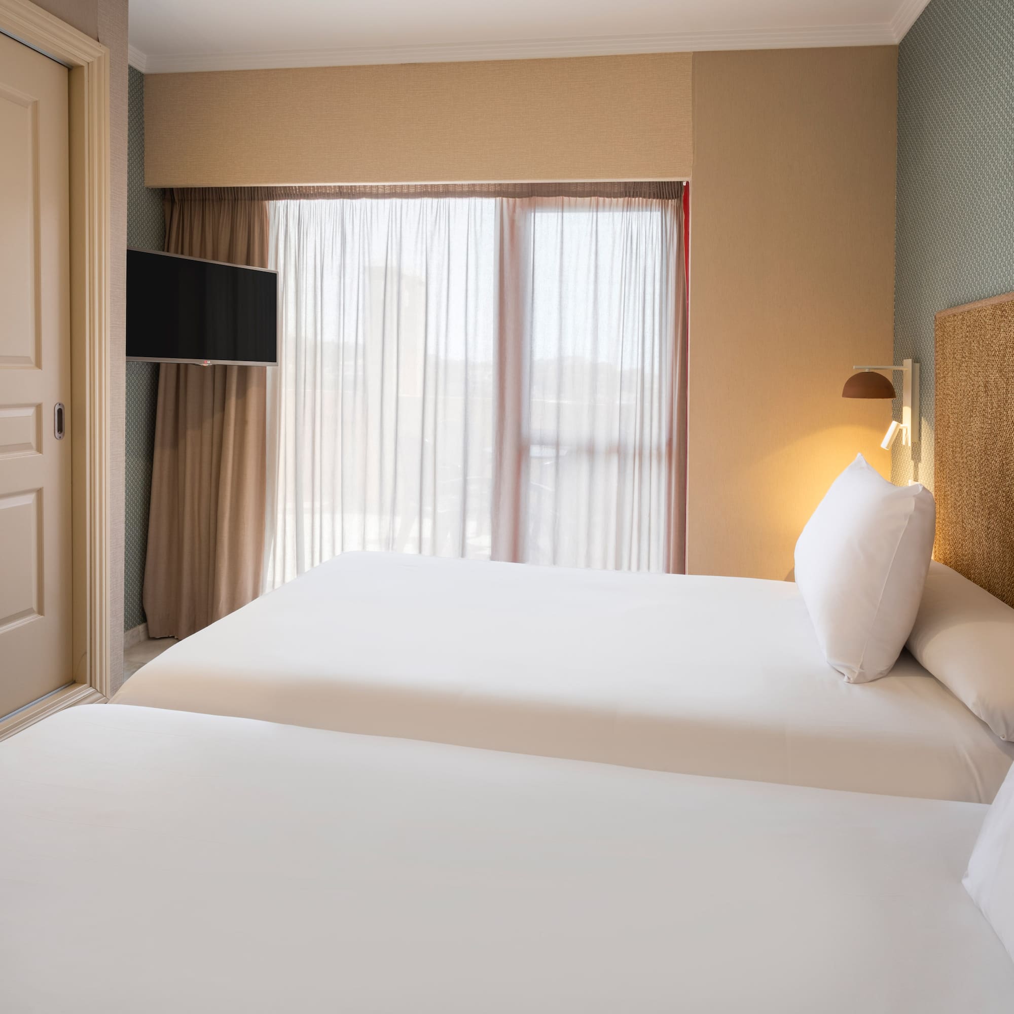 Hotel bedroom with twin beds, white linen, woven headboard, and wall TV.