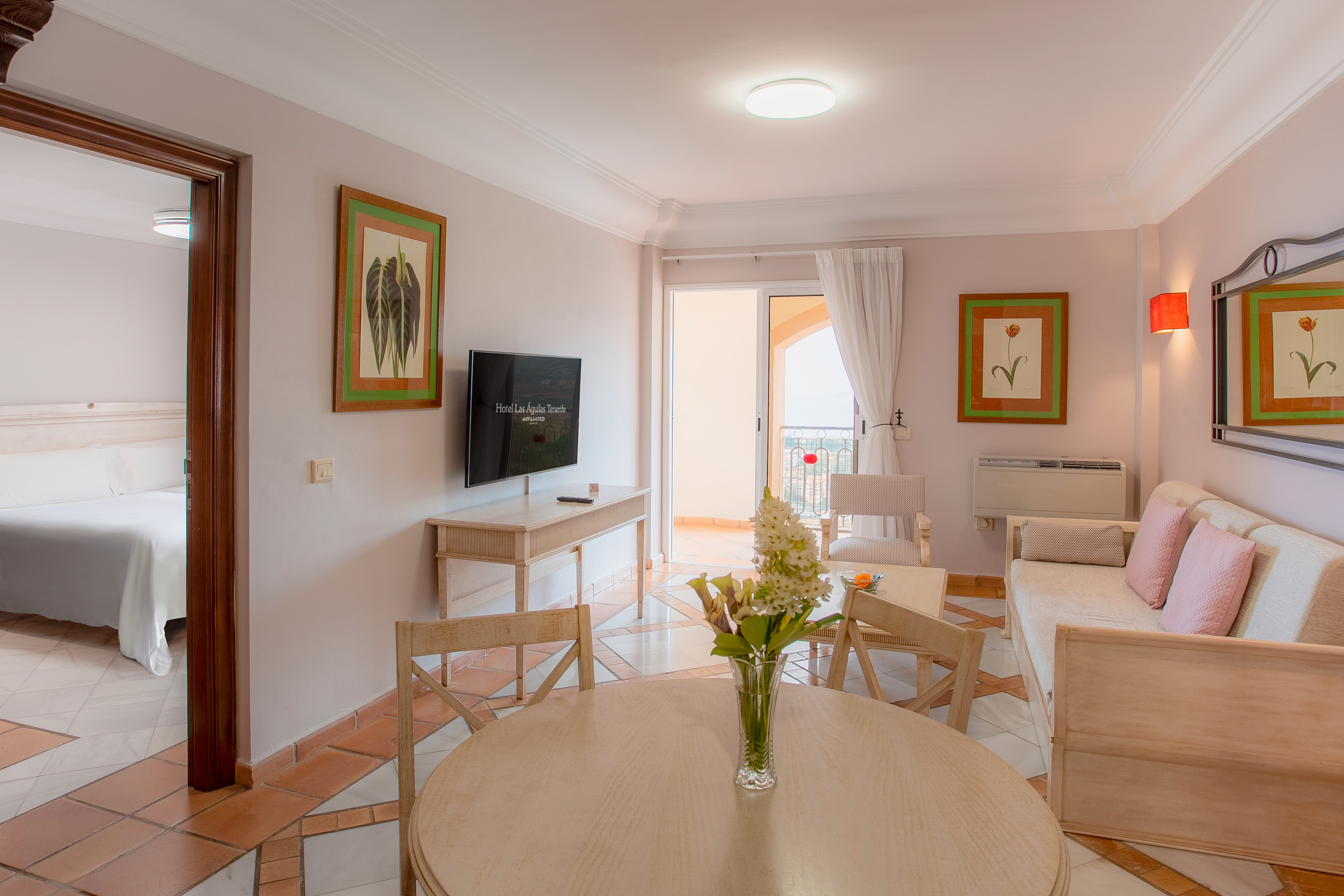 Tenerife hotel suite living room with dining area, TV, and balcony.