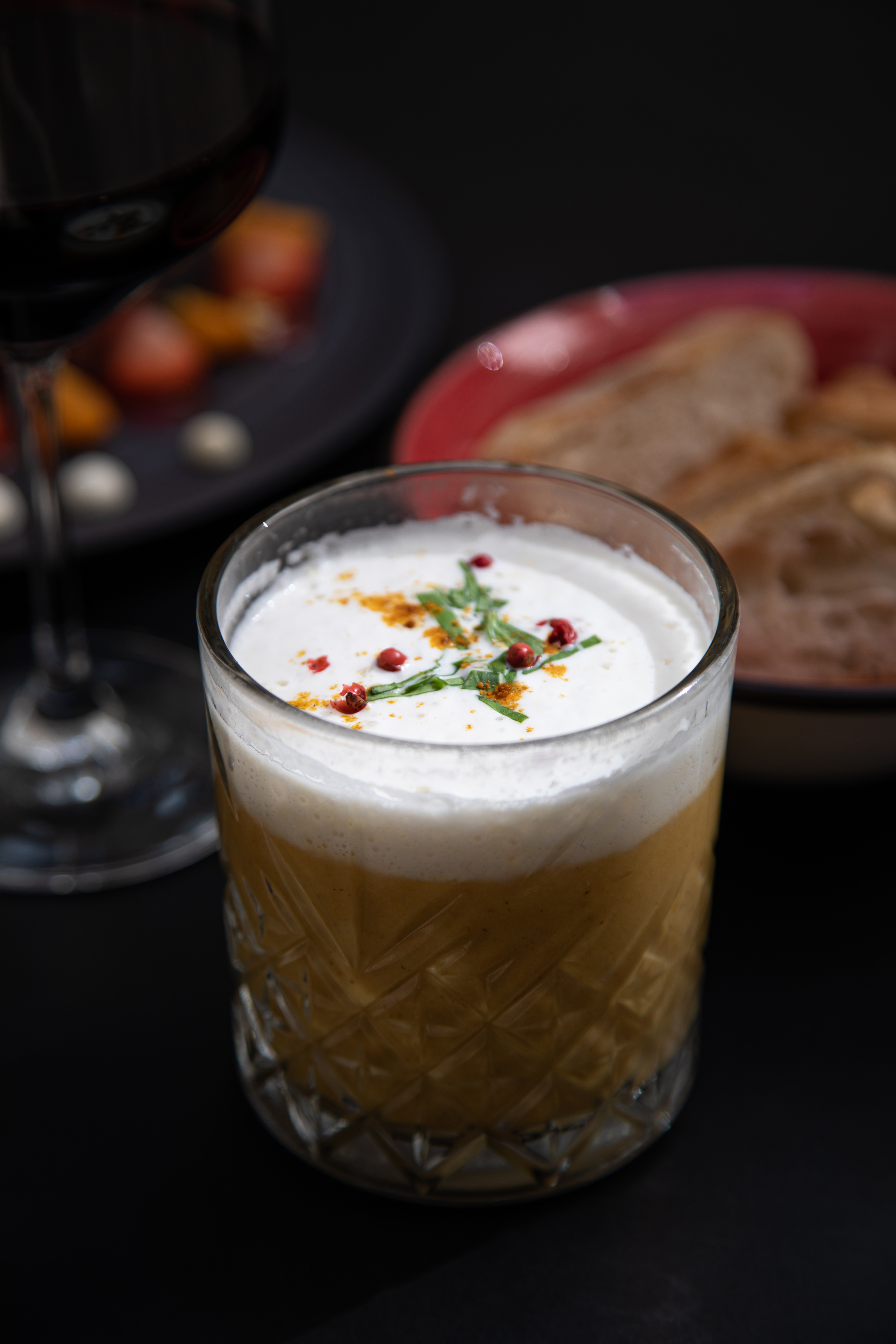 Creamy soup in patterned glass, garnished with red peppercorns, herbs, and spice.