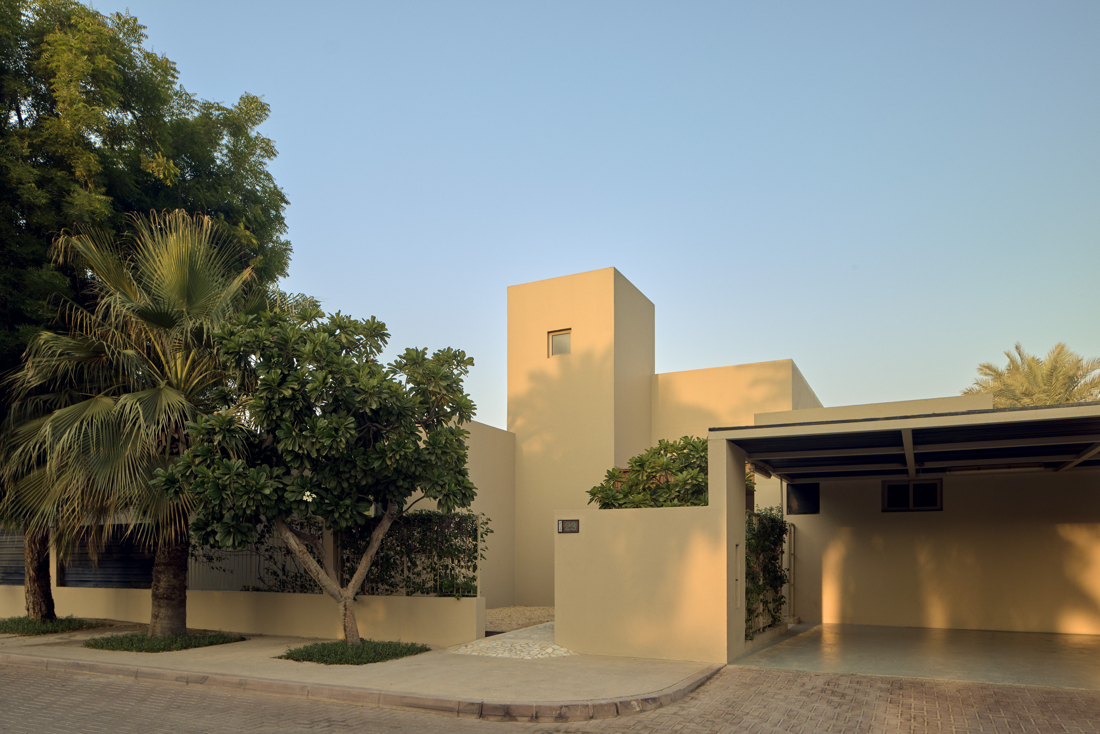 Modern residential architecture: beige minimalist house with tropical trees & carport.