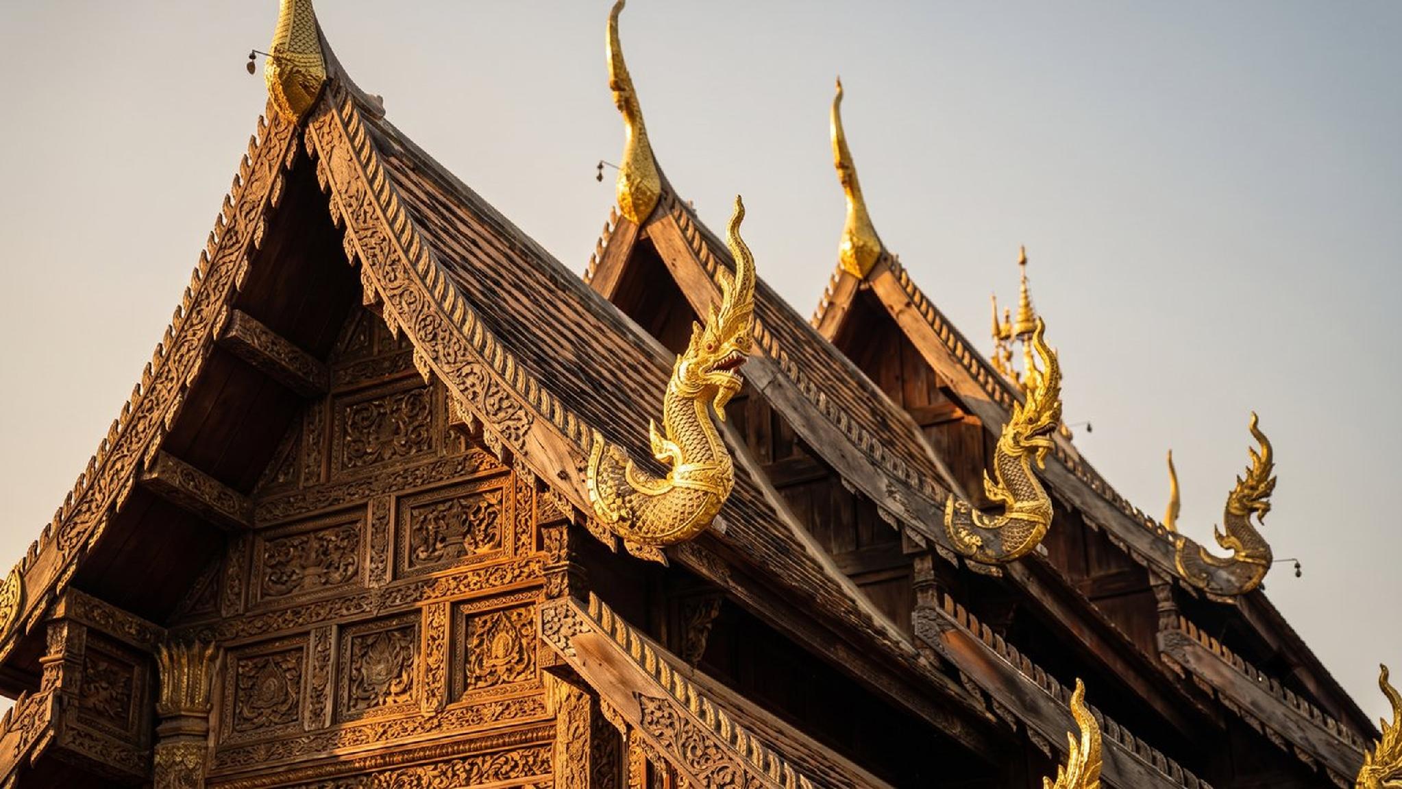 Golden Naga finials on a carved wooden Thai temple roof.