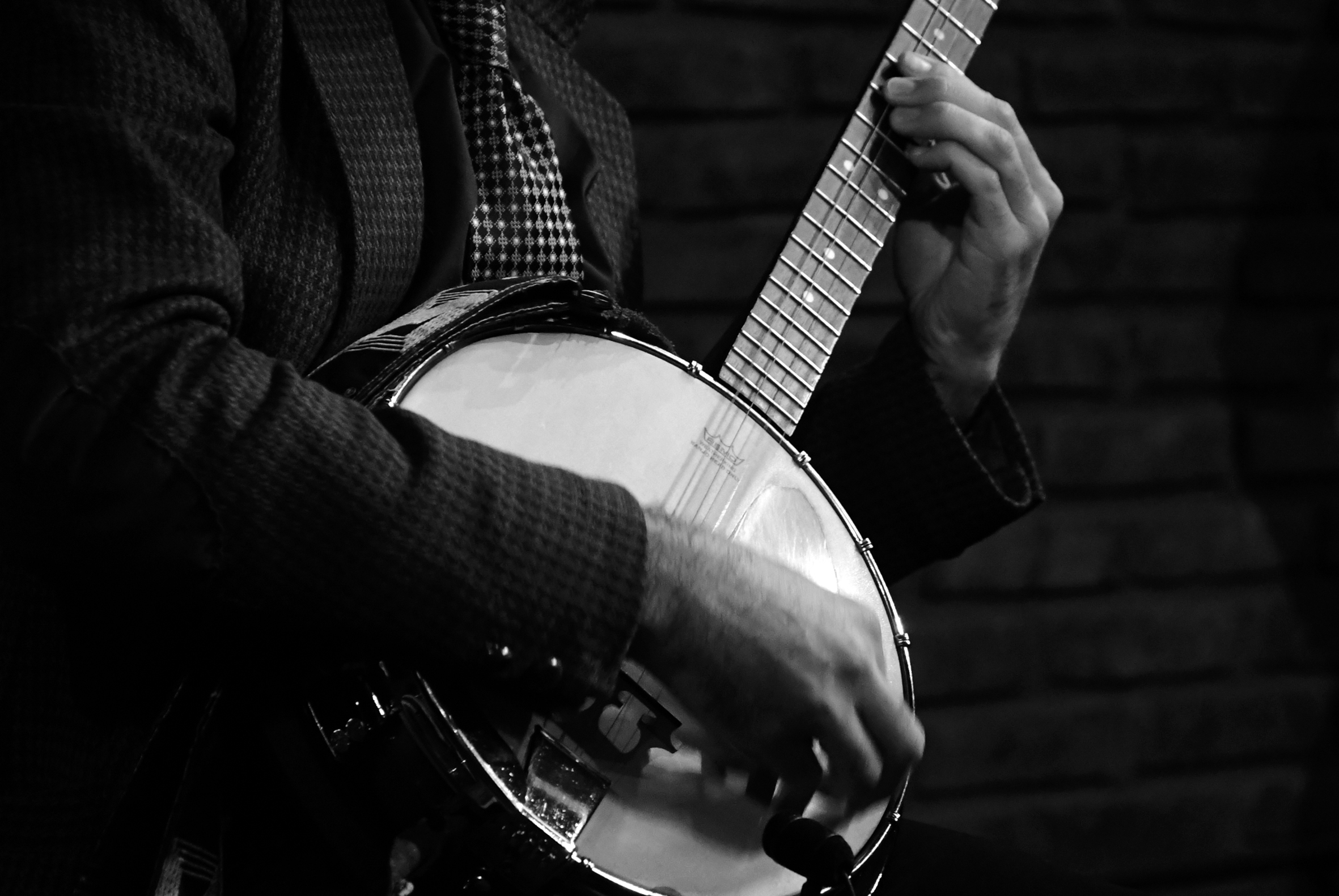 Músico tocando banjo en blanco y negro, detalle de manos y traje.